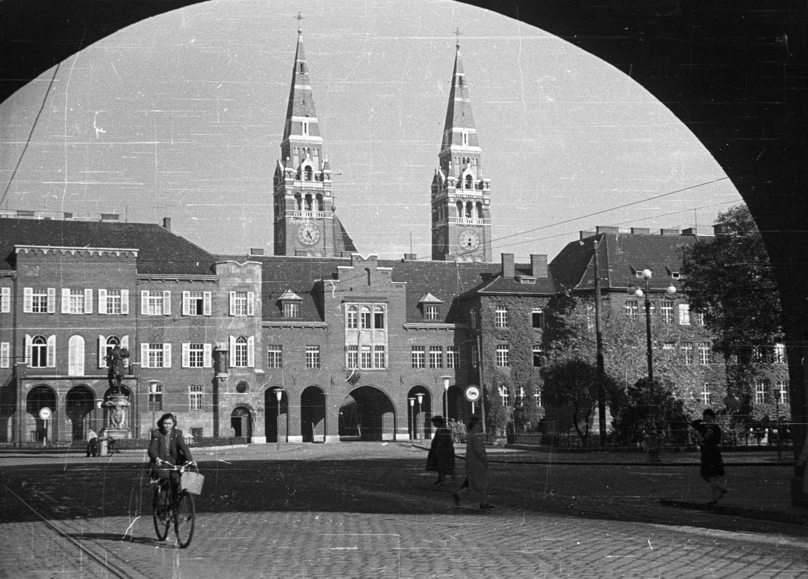 Hungary, Szeged, Aradi vértanúk tere a Hősök kapujától nézve. Az egyetem épületei mögött a Fogadalmi templom tornyai., 1953, Kollár Balázs, bicycle, gate, Frigyes Schulek-design, tower, Cathedral, Fortepan #101216