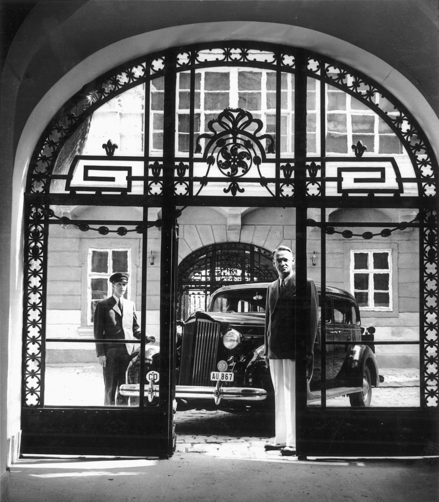 Magyarország, budai Vár, Budapest I., Táncsics Mihály (Verbőczy) utca 1., kapualja, a korábbi brit követség udvarán szemben Carl Lutz svájci diplomata., 1943, Archiv für Zeitgeschichte ETH Zürich / Agnes Hirschi, Carl Lutz, sofőr, rendszám, Packard-márka, kovácsoltvas kapu, Budapest, sofőrsapka, diplomata jelzés, Fortepan #105639