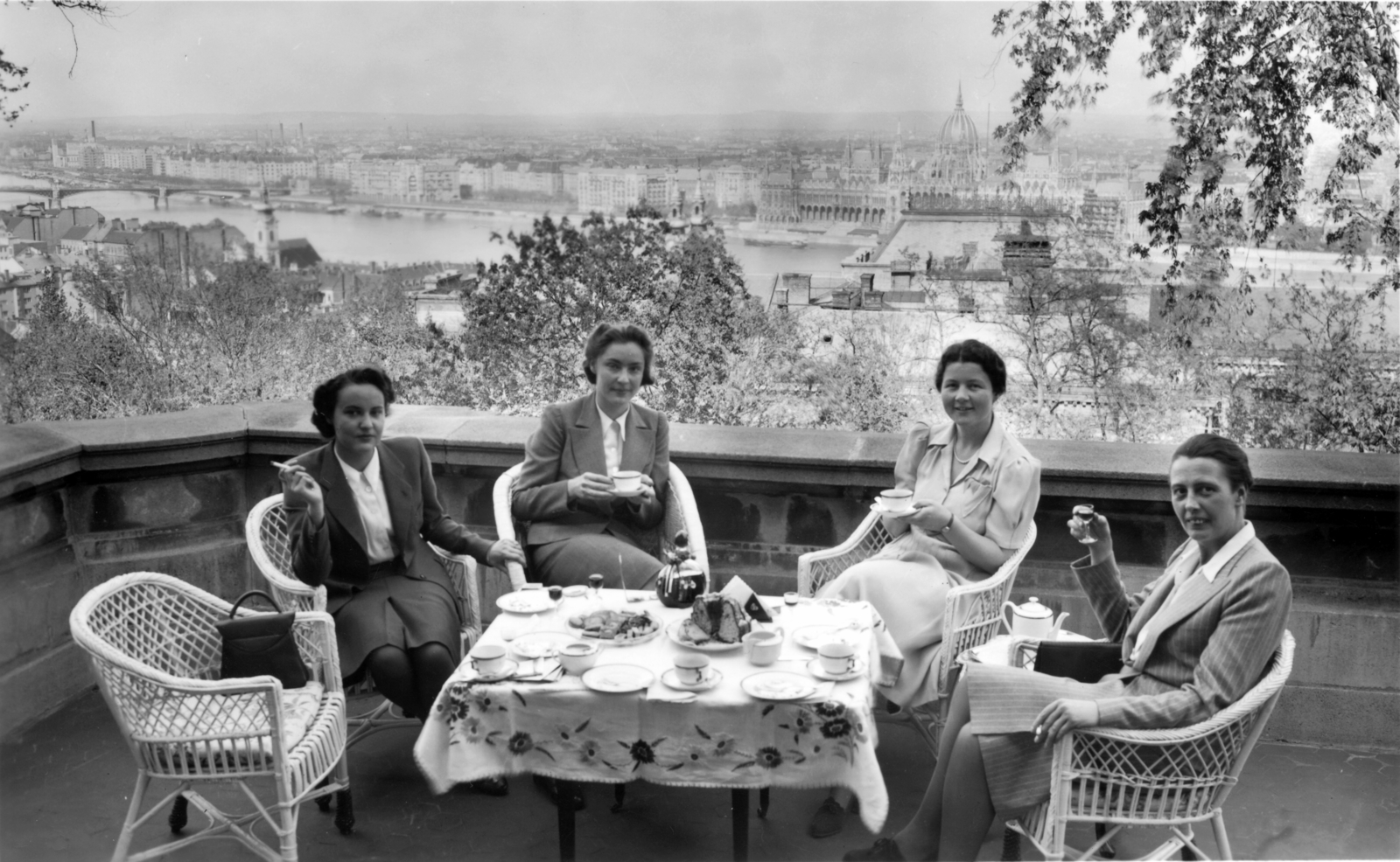 Magyarország, budai Vár, Budapest I., Táncsics Mihály (Verbőczy) utca 1., a korábbi brit követség épületének terasza, kilátás a Duna és a Parlament felé. A bécsi svájci konzulátus titkárnői látogatóban Budapesten., 1943, Archiv für Zeitgeschichte ETH Zürich / Agnes Hirschi, Carl Lutz, fonott szék, terasz, teáskanna, kuglóf, Budapest, Fortepan #105761
