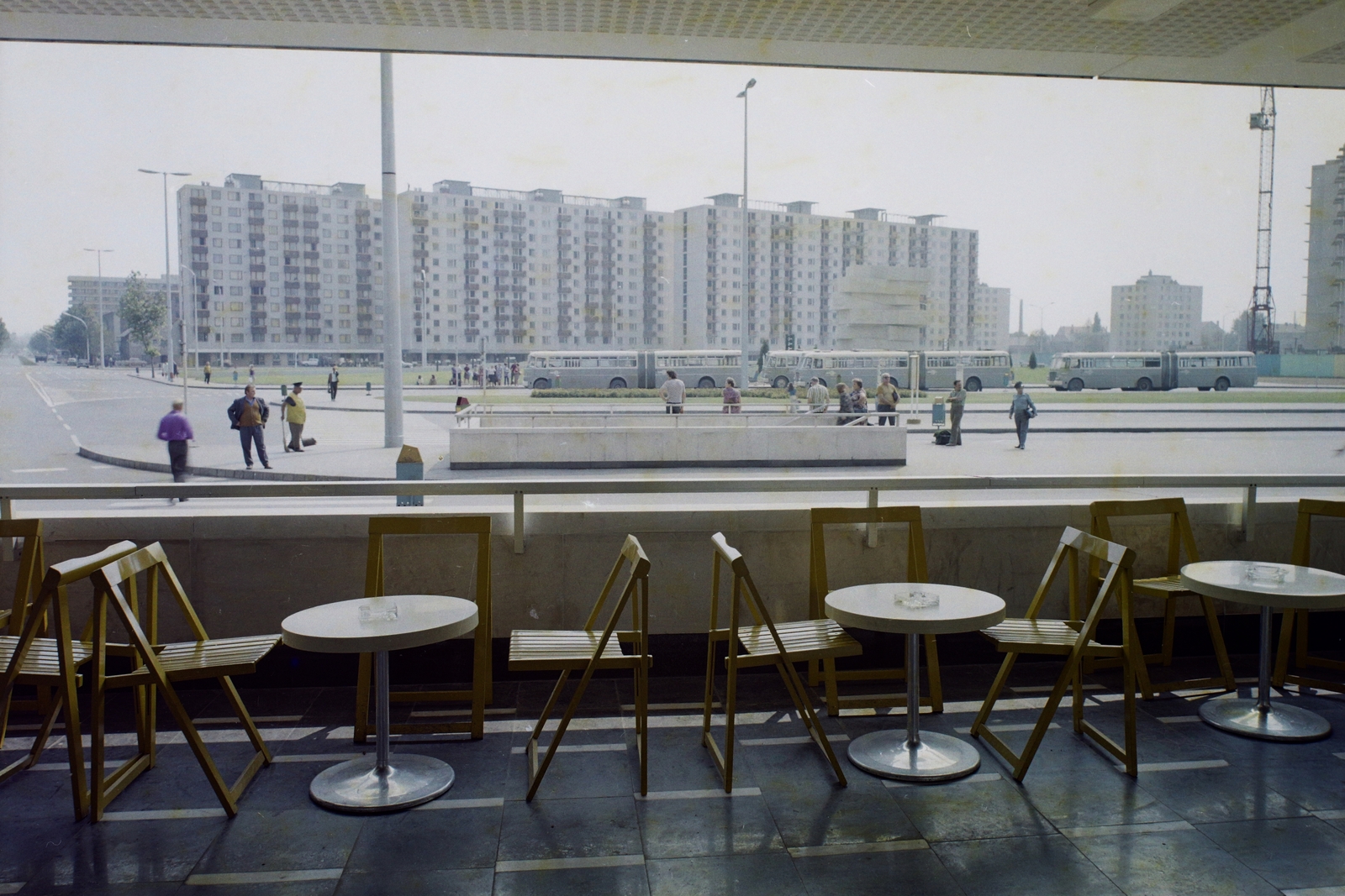 Magyarország, Szolnok, presszó a vasútállomáson. Szemben a Jubileum téren Gyurcsek Ferenc és Kampis Miklós alkotása a Tanúhegy (1975), ami a város 900 éves fennállásának emlékére készült., 1975, Bauer Sándor, színes, életkép, terasz, utcaseprő, Ikarus 620/630, autóbuszállomás, Ikarus 620 csuklós, autóbusz, Ikarus-márka, közvilágítás, emlékmű, panelház, asztal, daru, szék, szemetes, Fortepan #109825