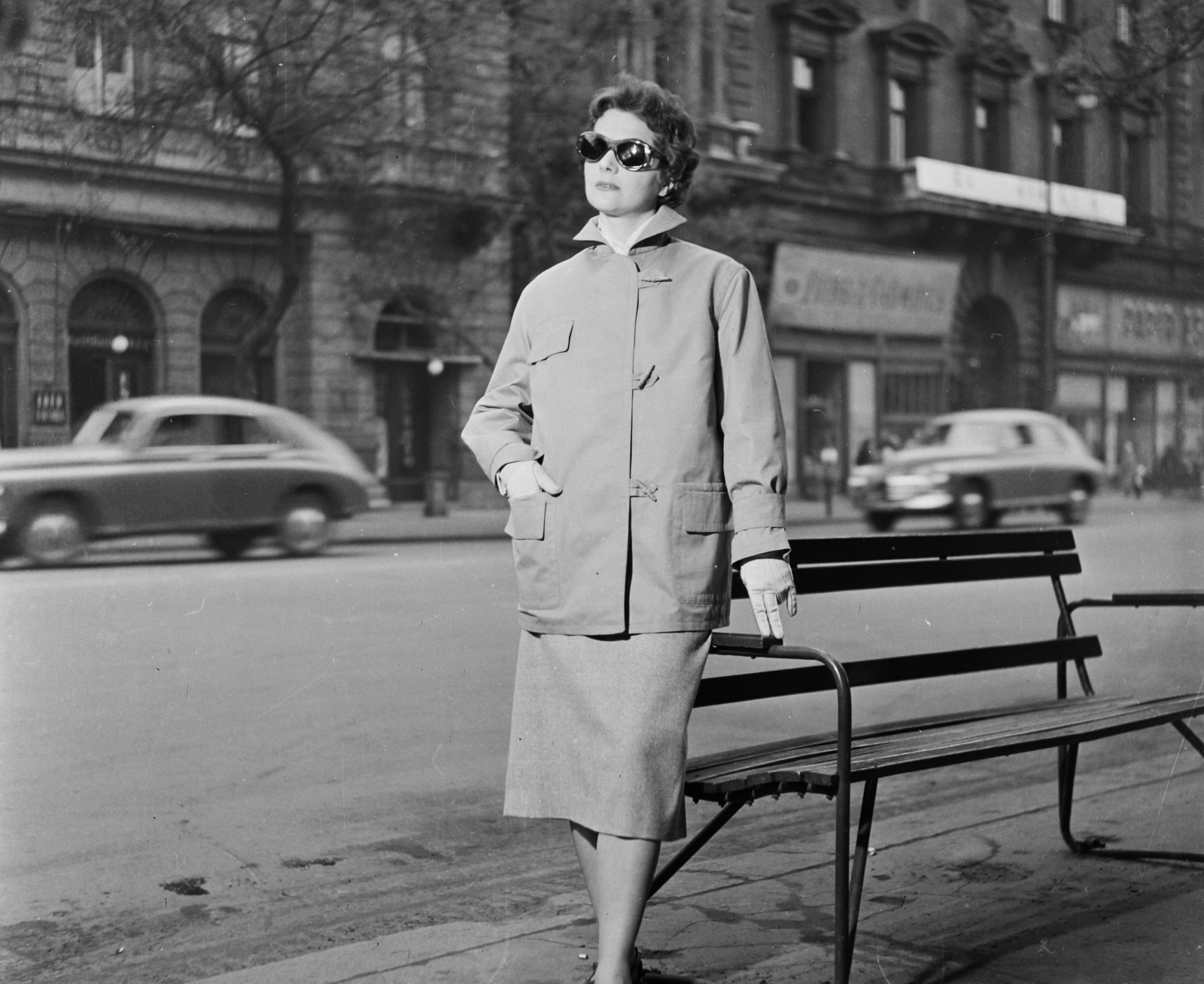 Magyarország, Budapest VI., Andrássy út (Népköztársaság útja), szemben az 5-ös és 3-as számú ház. Vitéz Eszter manöken, 1957, Bauer Sándor, divat, utcabútor, utcakép, napszemüveg, pad, GAZ M20 Pobeda, manöken, Budapest, híres ember, Fortepan #110342