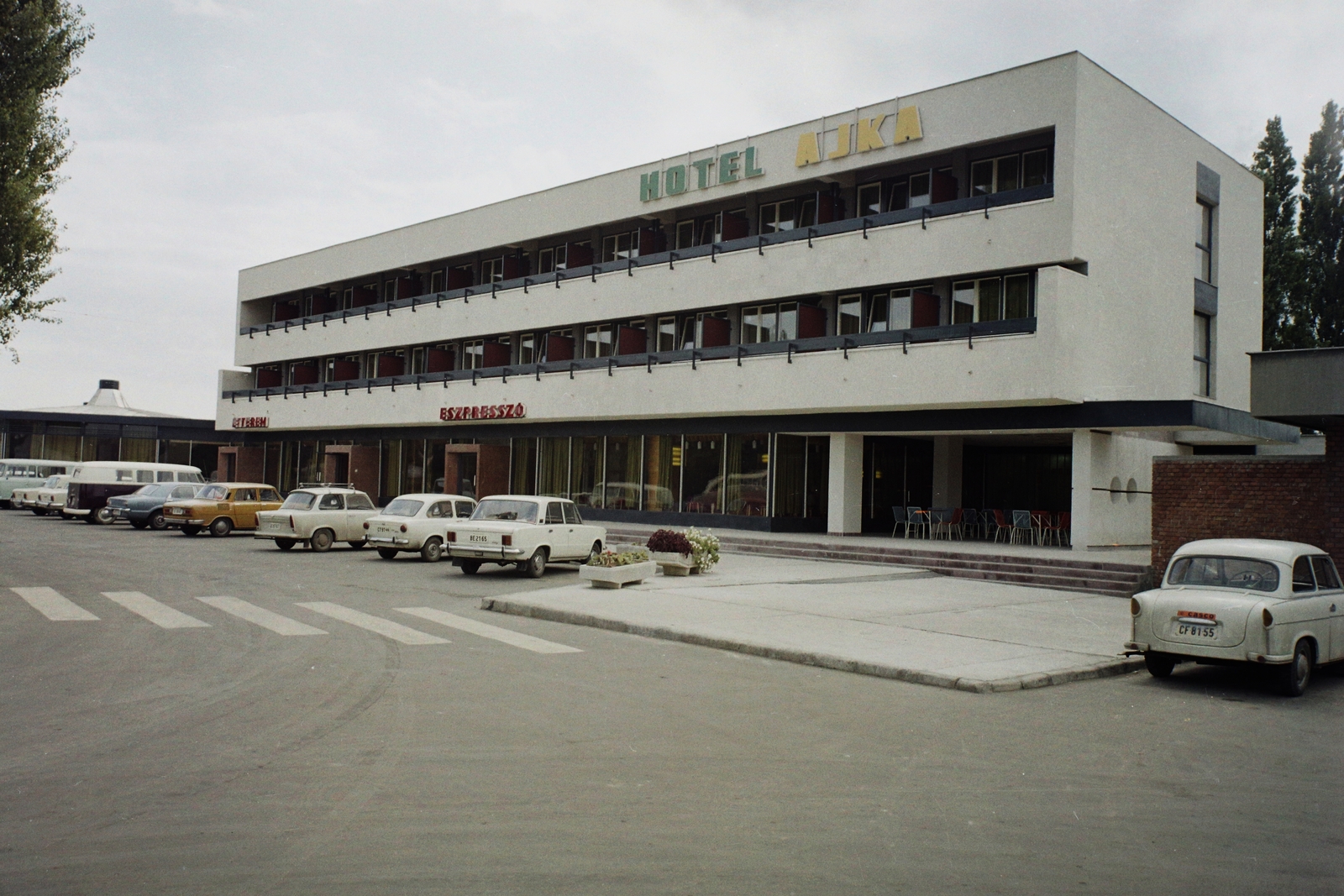 Magyarország, Ajka, Szabadság tér 8., Hotel Ajka., 1974, Bauer Sándor, színes, Trabant-márka, Barkas-márka, Trabant 601, rendszám, Skoda 100, Fiat 850, Trabant 600, Polski Fiat 125p, neon felirat, Volkswagen Transporter 2, Ford Taunus TC, Fortepan #112320