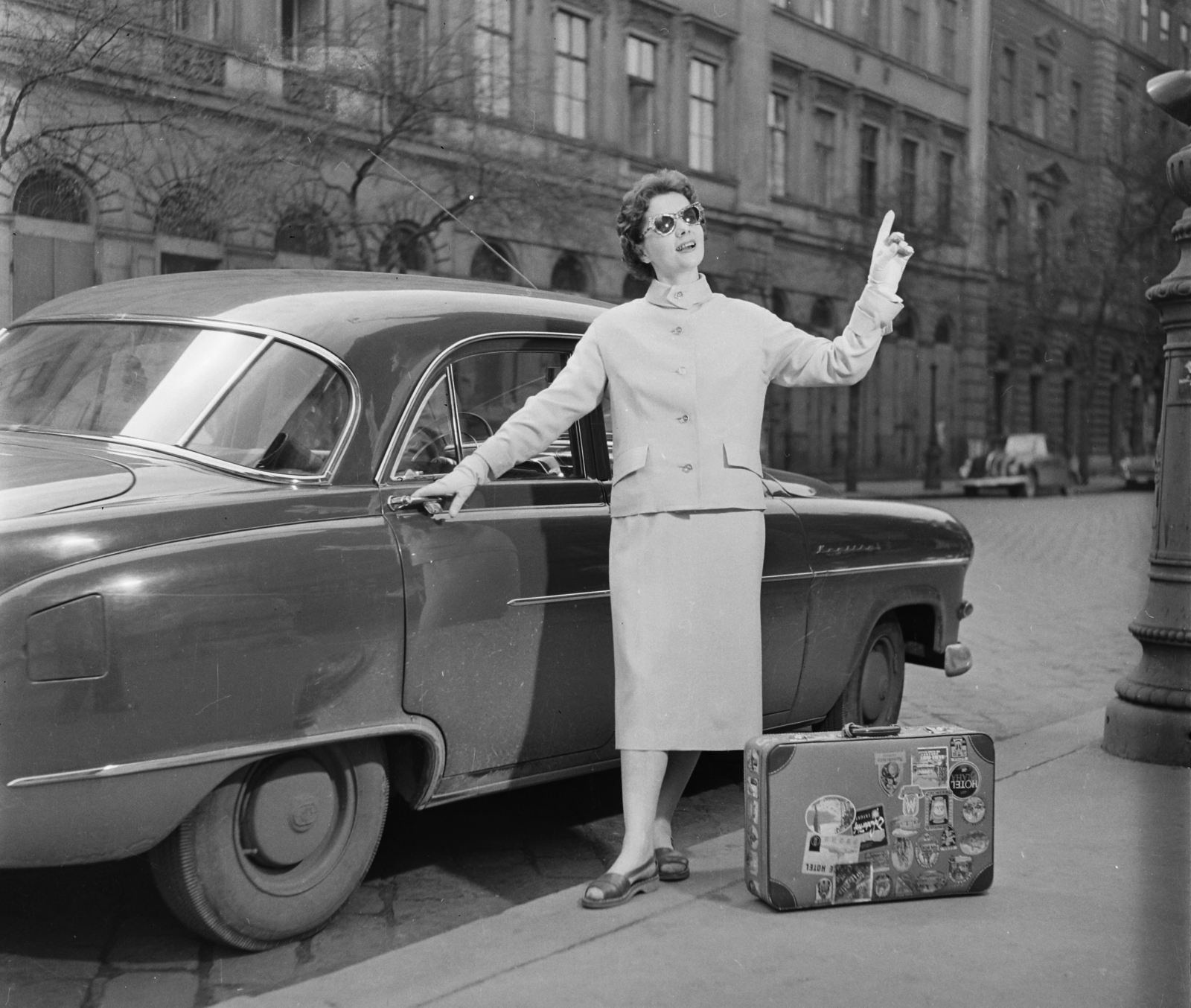 Hungary, Budapest V., a Szent István tér déli oldala. Vitéz Eszter manöken egy Opel Kapitän személygépkocsi mellett áll., 1957, Bauer Sándor, fashion, suitcase, Budapest, suitcase stickers, girls'n'cars, Fortepan #112896