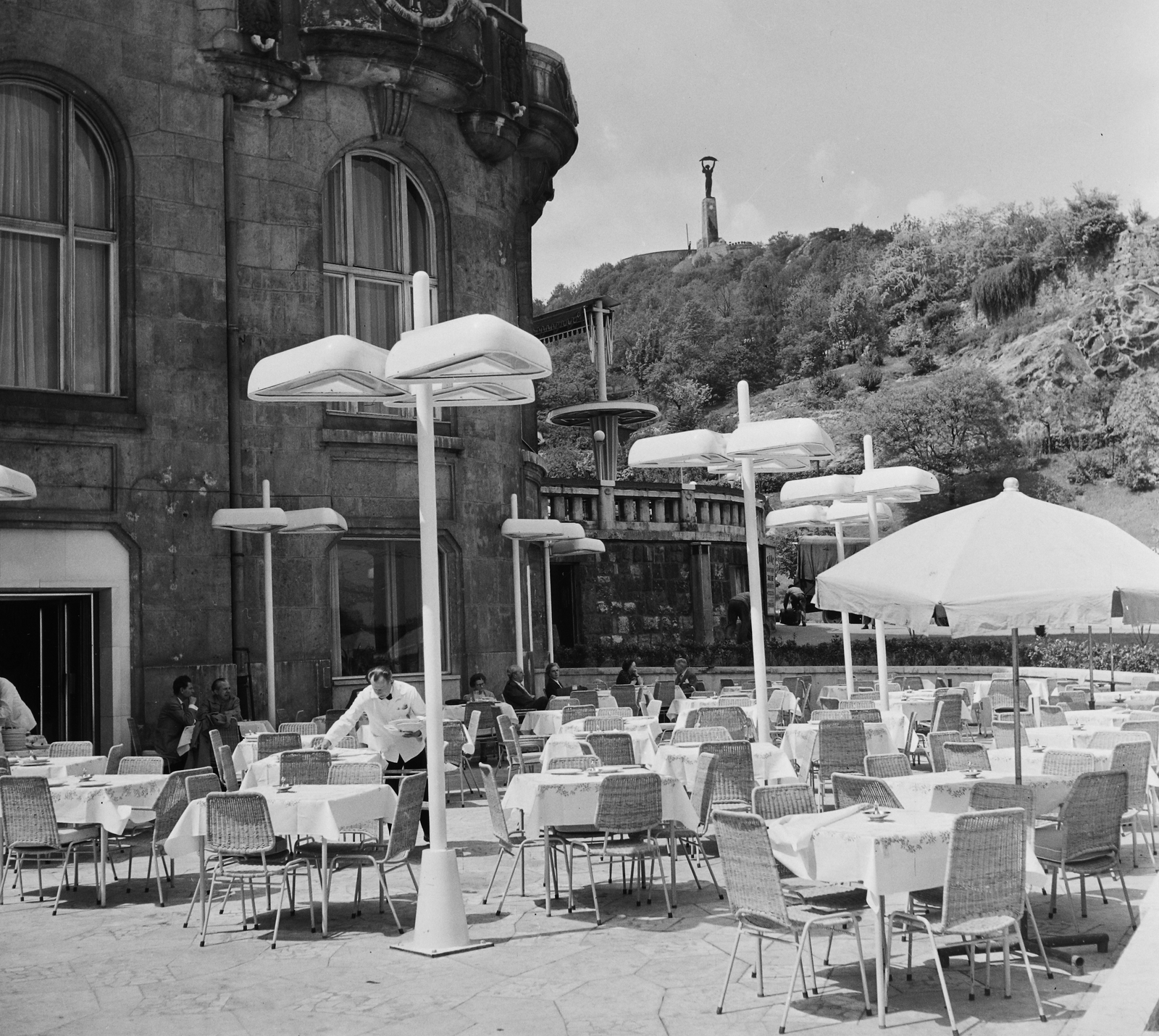 Magyarország, Budapest XI., Gellért Szálló, terasz. Fenn a Gellért-hegyen a Citadella és a Felszabadulási Emlékmű., 1962, Bauer Sándor, lámpa, napernyő, terasz, Budapest, Fortepan #113927