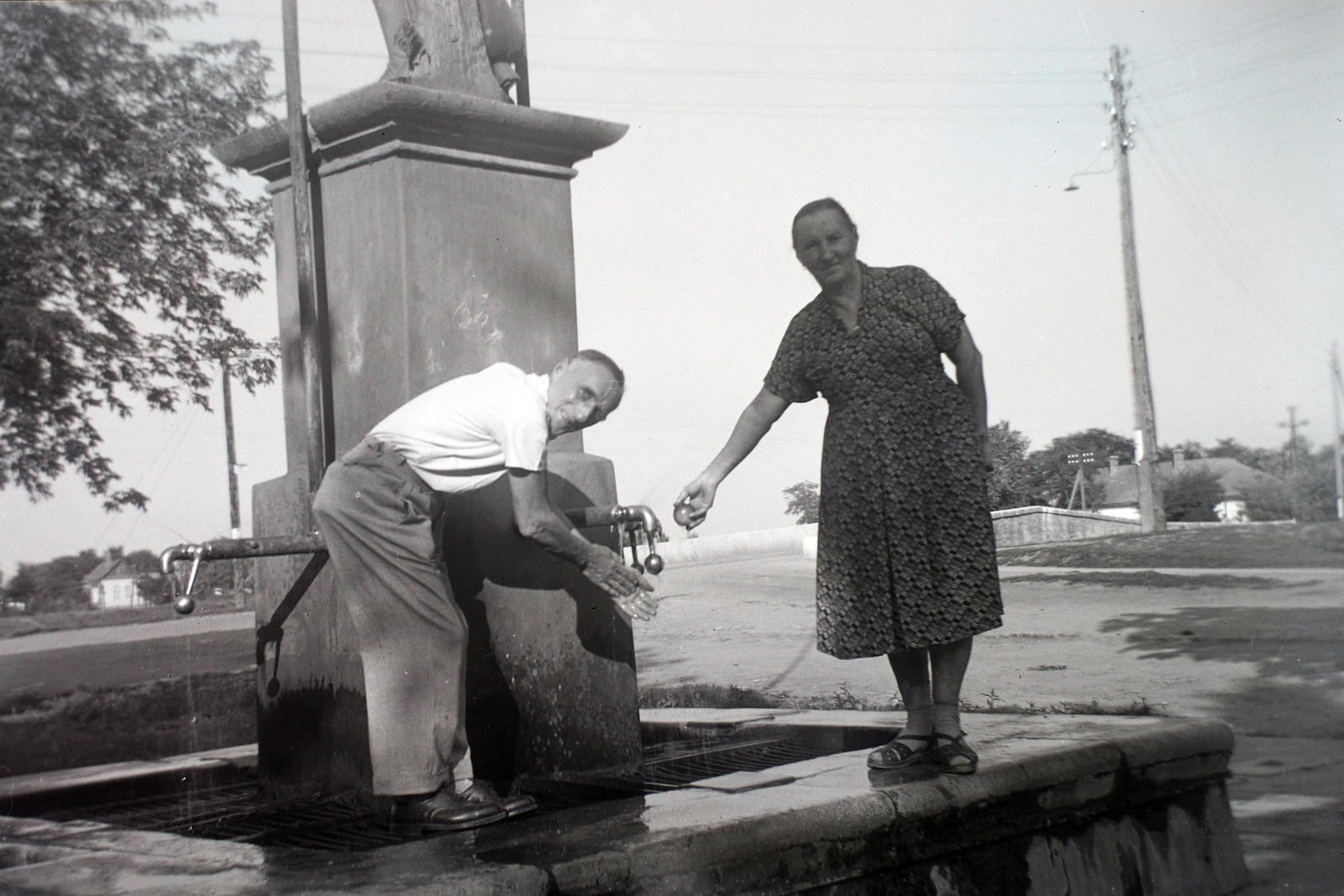 Hungary, Jászdózsa, Dózsa György tér, artézi kút, háttérben a Kőhíd a Holt-Tarna (Tarna)-n., 1939, Fortepan/Album009, hand wash, looking back, public well, Fortepan #116431