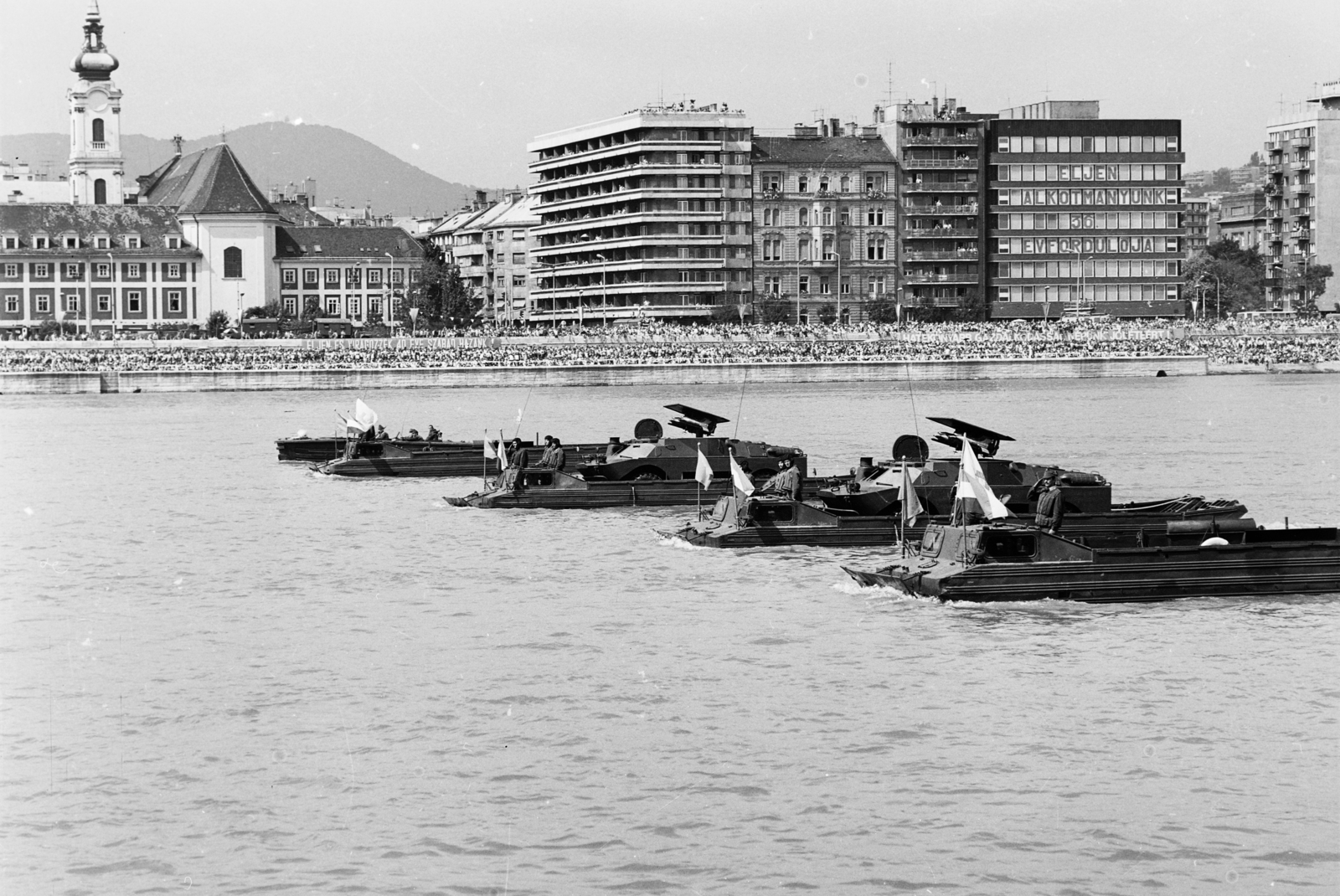 Magyarország, Budapest I.,Budapest II., augusztus 20-i vízi- és légiparádé a Dunán, szemben a Bem rakpart, balra a Szent Ferenc sebei templom és az egykori ferences kolostor, mellette a Csalogány utca torkolata., 1985, MHSZ, templom, zászló, felirat, honvédség, augusztus 20, harcjármű, magyar katona, Budapest, vízi parádé, BRDM-1, Fortepan #118433