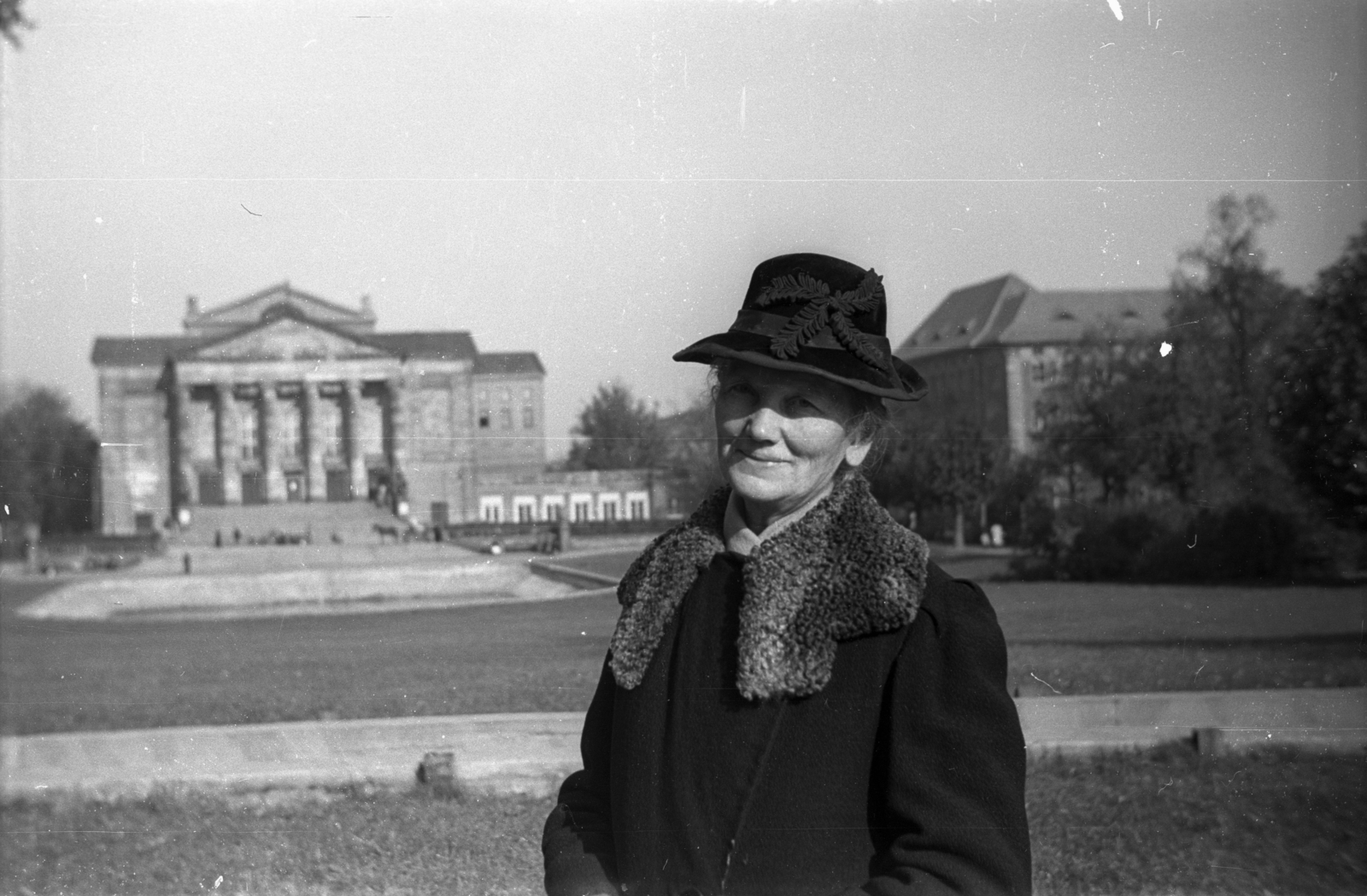 Lengyelország, Poznań, Mickiewicz park, a háttérben balra a Nagyszínház (Teatr Wielki im. Stanisława Moniuszki), jobbra a Karol Marcinkowski Orvosi Egyetem., 1948, Bogdan Celichowski, kalap, kabát, mosoly, hölgy, Fortepan #119221