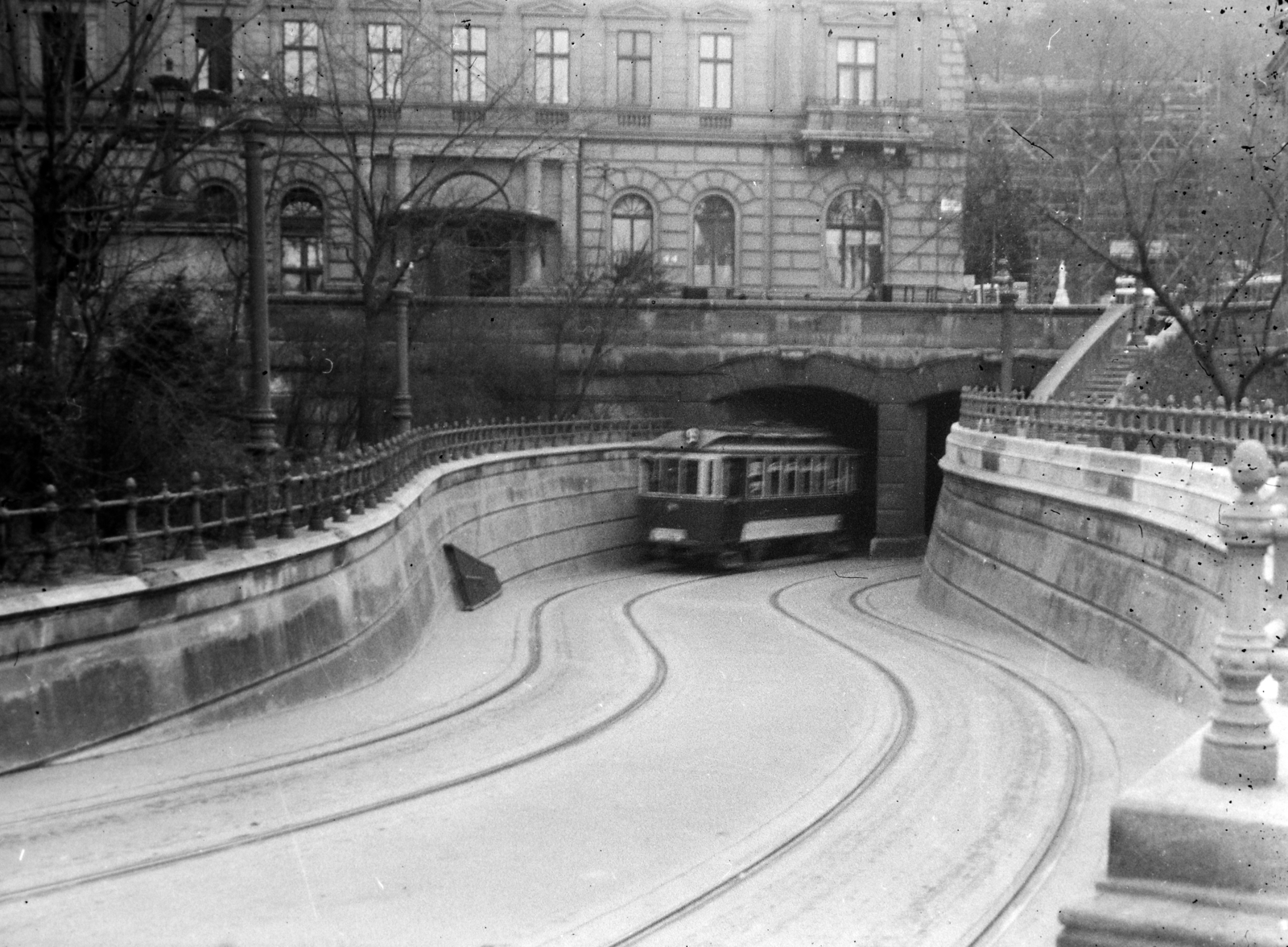 Hungary, Budapest I., villamos alagút a Széchenyi Lánchíd budai hídfője alatt a Lánchíd utca felől nézve. Szemben a Kereskedelmi Minisztérium háború során megsérült majd lebontott épülete (Lánchíd utca 1-3.), előtte a 0 km-t jelző szobor (Patrona Hungariae), mögötte az Alagút látszik., 1940, Dienes Balázs, railing, tram, underpass, Budapest, Fortepan #120291