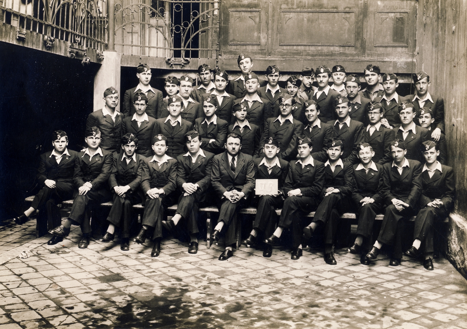 Hungary, Budapest II., Frankel Leó út (Zsigmond utca) 114., Magyar Királyi Állami Árpád Reálgimnázium (később Budapest III., Nagyszombat utca 19., Árpád Gimnázium), csoportkép egy hatodikos osztályról., 1939, Hanser Mária, uniform, class photo, tableau, sitting with hands on knees, open-necked shirt, leg over leg, Bocskai-jacket, teacher, badge on a lapel, student, badge, Budapest, Fortepan #120654