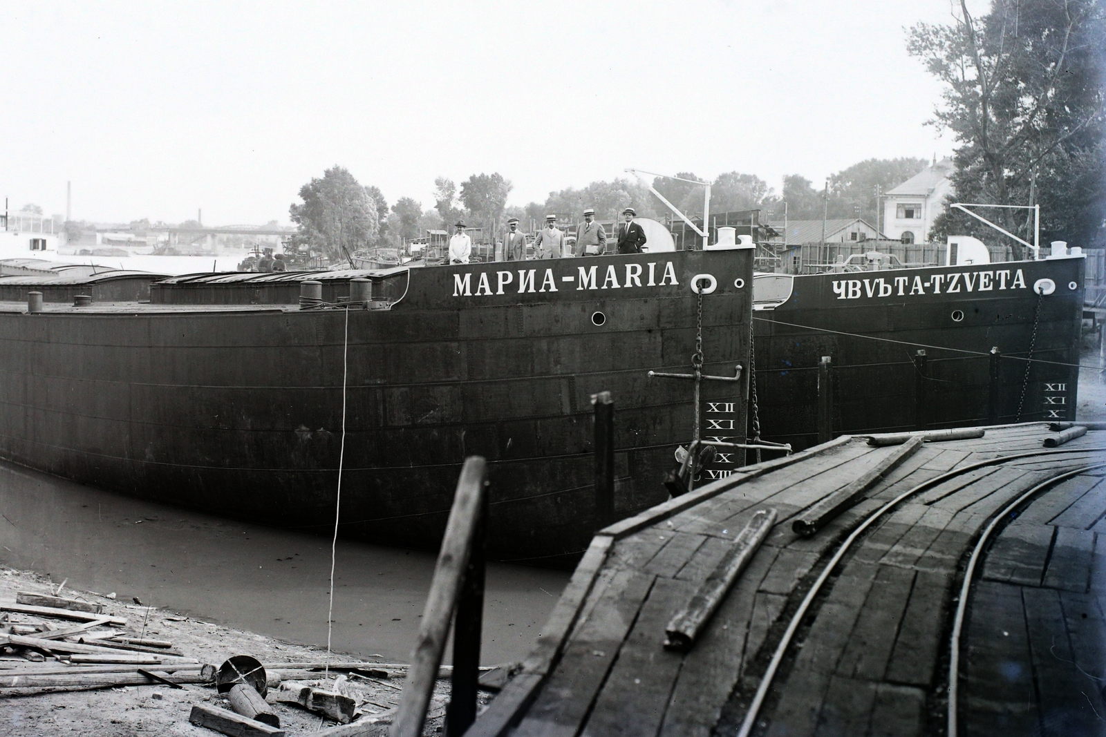 Magyarország, Budapest XIII., Újpesti-öböl, balra a háttérben az Újpesti vasúti híd. Ganz és Tsa. Danubius Gép-, Waggon- és Hajógyár Rt. Maria és Tzveta uszályok, fedélzetükön mérnökök és üzemvezetők., 1925, Magyar Műszaki és Közlekedési Múzeum / Történeti Fényképek Gyűjteménye / Óbudai Hajógyár gyűjteménye, uszály, Budapest, cirill írás, kétnyelvű felirat, római számok, Fortepan #122008