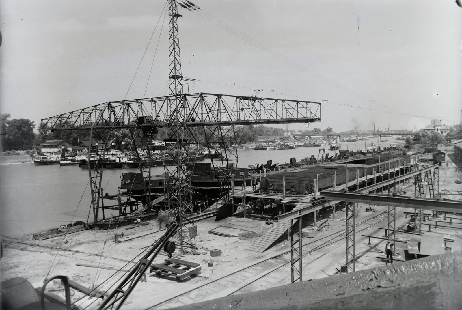 Hungary, Budapest XIII., Újpesti-öböl, Ganz és Tsa. Villamossági-, Gép-, Waggon- és Hajógyár Rt. Shell tankuszályok építése és egy épülő uszálybárka. Balra a Népsziget, távolban az Újpesti vasúti híd. Leltári jelzet: MMKM TFGY 2017.1.96., 1937, Magyar Műszaki és Közlekedési Múzeum / Történeti Fényképek Gyűjteménye / Ganz gyűjtemény, barge, Budapest, gantry crane, Fortepan #122540