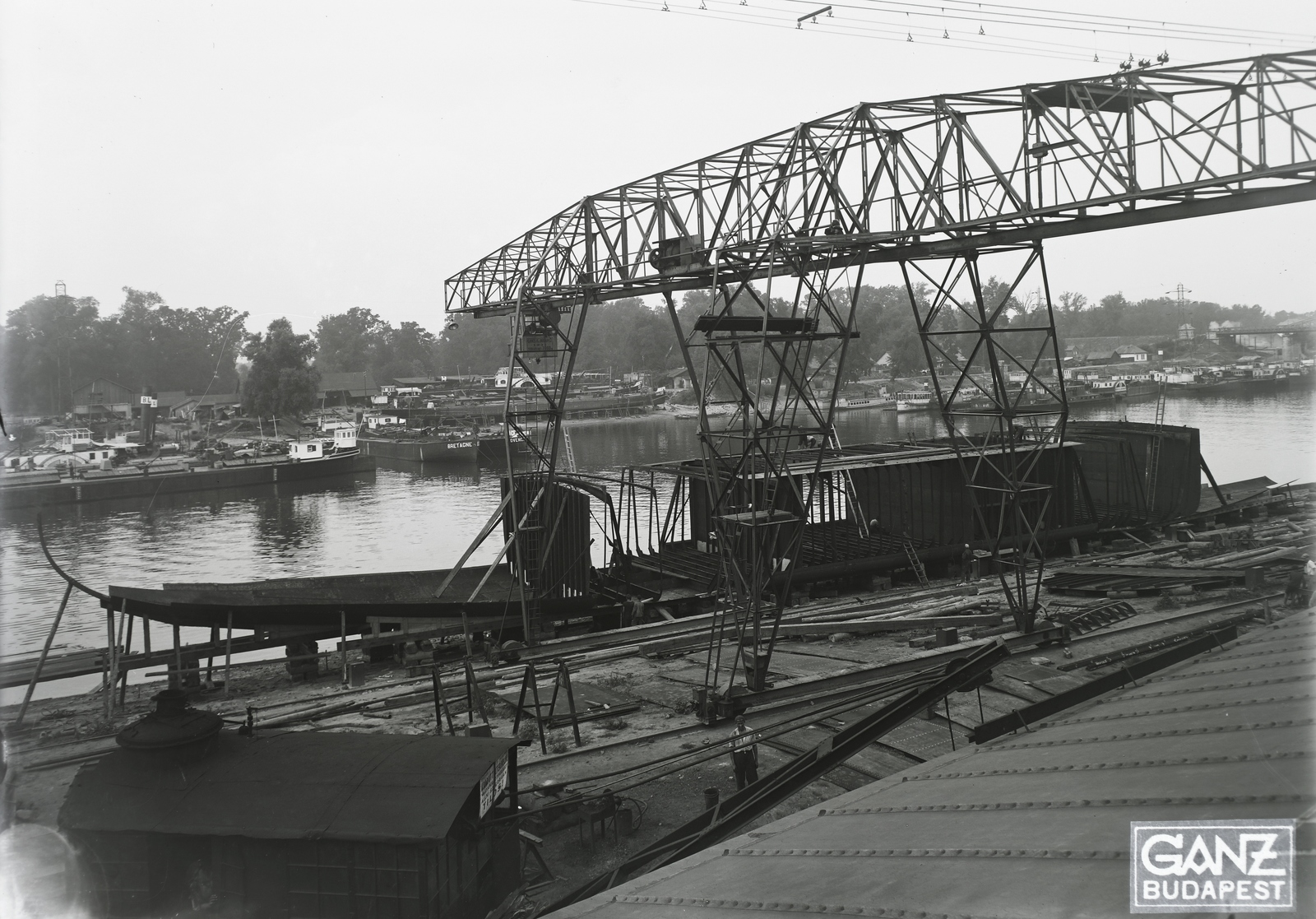 Hungary, »DTRT TISZA (1937) duna-tengeri áruszállító csavaros motorhajó építése a harmadik héten, háttérben a SFND BRETAGNE, SFND PROVENCE, háttérben CSD SAZAVA (1904).« Leltári jelzet: MMKM TFGY 2017.1.117., 1937, Magyar Műszaki és Közlekedési Múzeum / Történeti Fényképek Gyűjteménye / Ganz gyűjtemény, gantry crane, Fortepan #122553