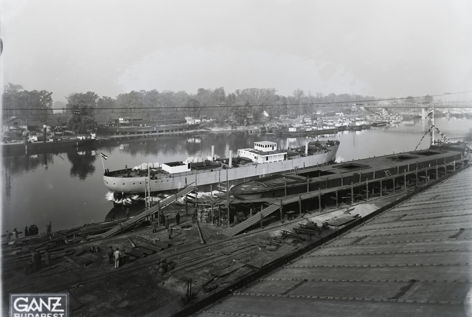 Hungary, Budapest XIII., Újpesti-öböl, jobbra az Újpesti vasúti híd. Ganz és Tsa. Villamossági-, Gép-, Waggon- és Hajógyár Rt. A DTRT Tisza (1937) Duna-tengerjáró áruszállító hajó vízre bocsátása. Leltári jelzet: MMKM TFGY 2017.1.204., 1937, Magyar Műszaki és Közlekedési Múzeum / Történeti Fényképek Gyűjteménye / Ganz gyűjtemény, Budapest, Fortepan #122602