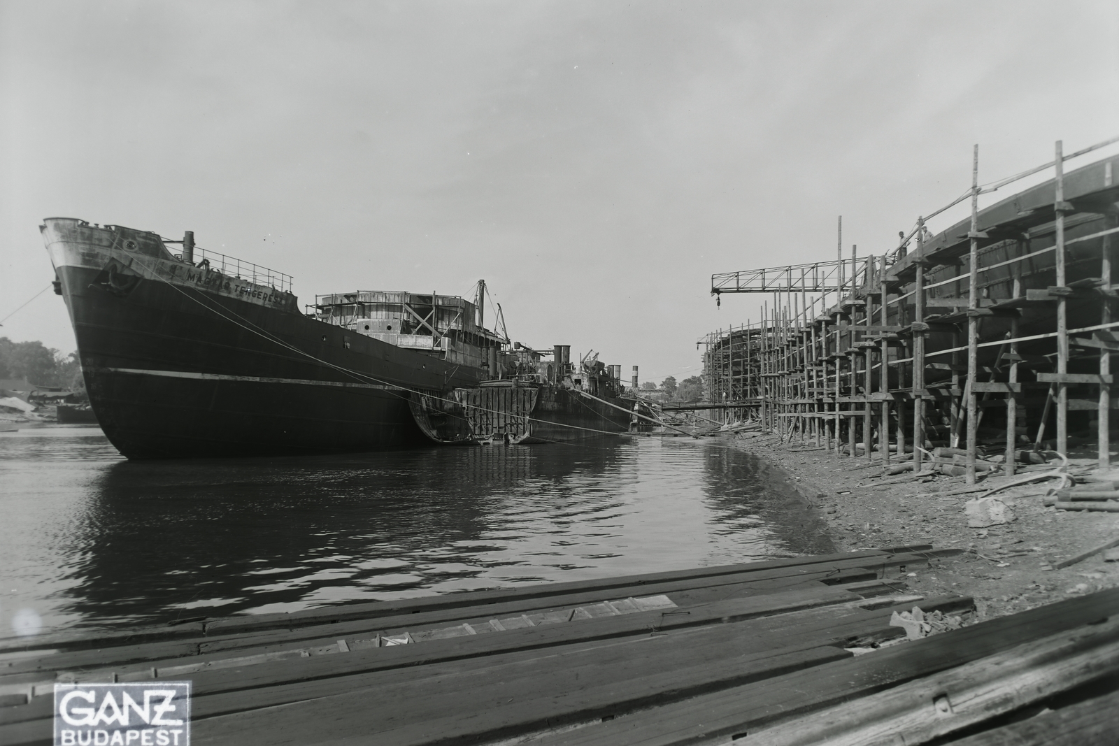 Magyarország, Budapest XIII., Újpesti-öböl, Ganz és Tsa. Villamossági-, Gép-, Waggon- és Hajógyár Rt., a Magyar Tengerész (1942) építése vízen, mellette a DTRT Kolozsvár (1941) roncsa. Leltári jelzet: MMKM TFGY 2017.1.852., 1943, Magyar Műszaki és Közlekedési Múzeum / Történeti Fényképek Gyűjteménye / Ganz gyűjtemény, Budapest, Fortepan #123114