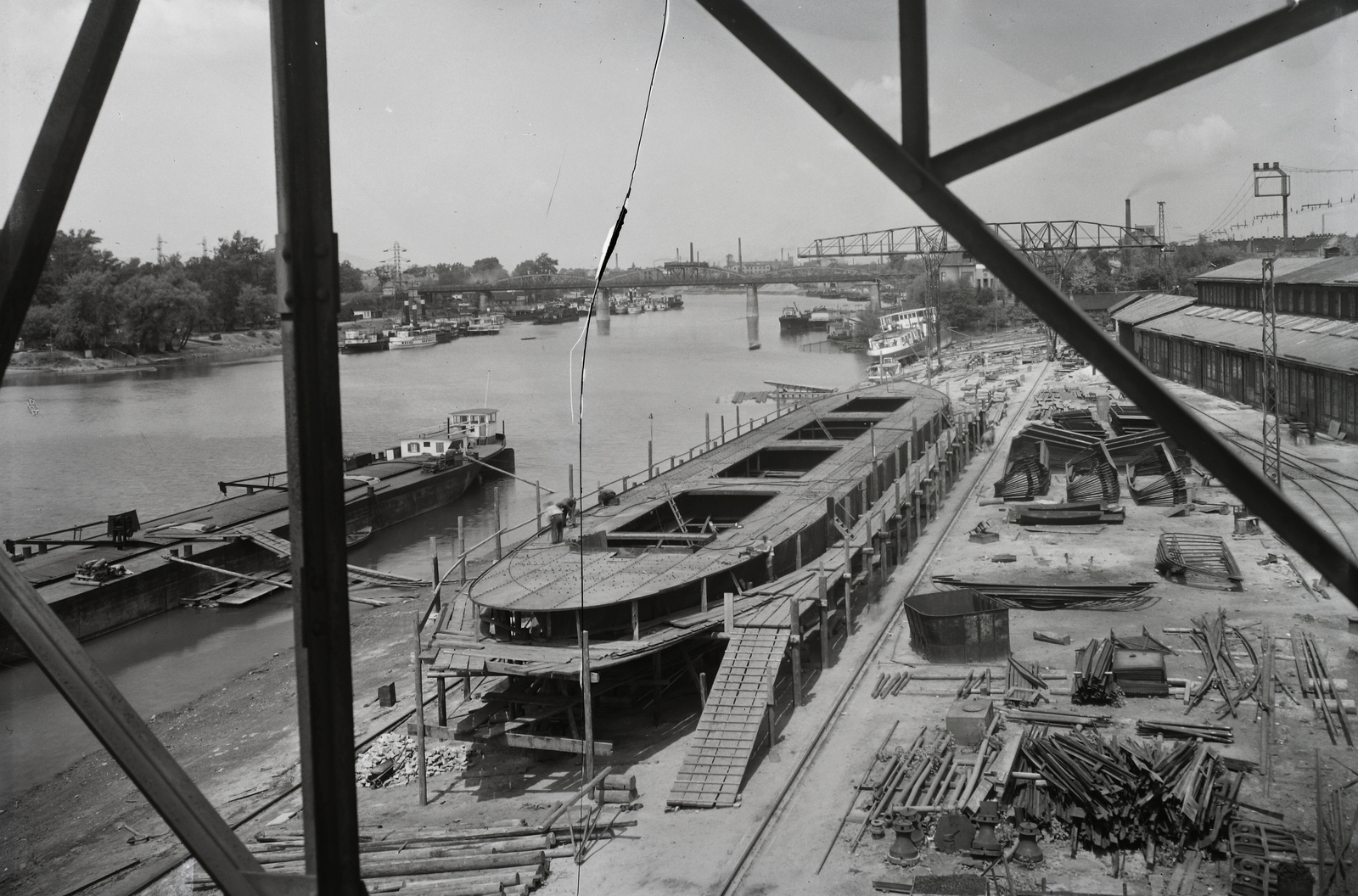 Hungary, Budapest XIII., Újpesti-öböl, a Ganz és Tsa. Villamossági-, Gép-, Waggon- és Hajógyár Rt. Háttérben az Újpesti vasúti híd. Épülő hajó a sólyán. Leltári jelzet: MMKM TFGY 2017.1.470., 1940, Magyar Műszaki és Közlekedési Múzeum / Történeti Fényképek Gyűjteménye / Ganz gyűjtemény, gantry crane, Budapest, Fortepan #123193