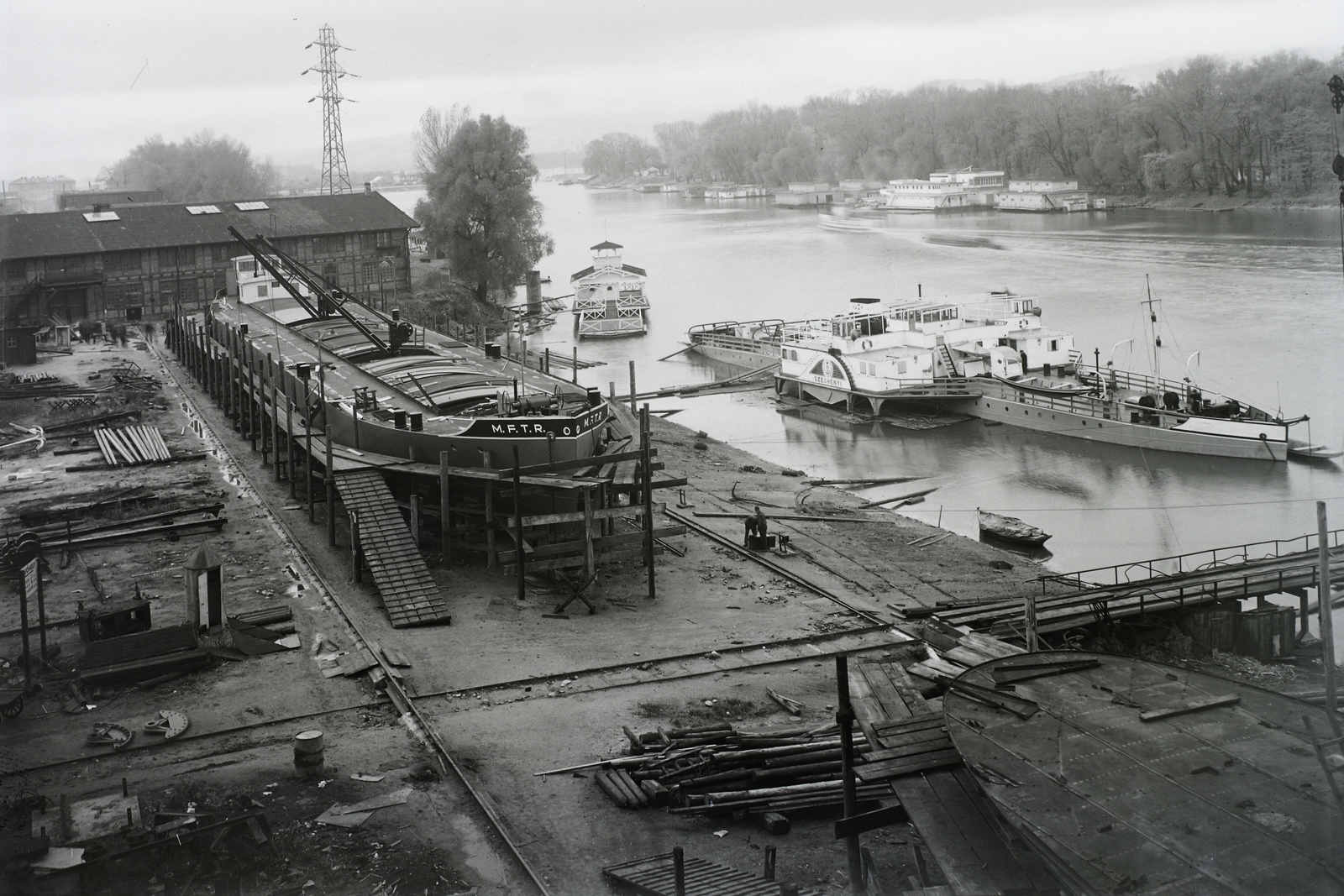 Magyarország, Budapest XIII., Újpesti-öböl, Ganz és Tsa. Villamossági-, Gép-, Waggon- és Hajógyár Rt. Épülő MFTR uszály a sólyán, mellette a vízen az MFTR Széchenyi (1938) dízel-elektromos vontatóhajó. Leltári jelzet: MMKM TFGY 2017.1.466., 1939, Magyar Műszaki és Közlekedési Múzeum / Történeti Fényképek Gyűjteménye / Ganz gyűjtemény, uszály, Budapest, Fortepan #123204