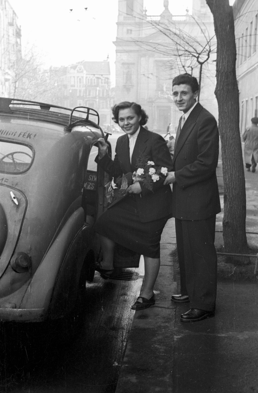 Hungary, Budapest VIII., a felvétel a Baross utca 63-67., a Kerületi Tanács (később Polgármesteri Hivatal) előtt készült. Háttérben a Horváth Mihály téren a Szent József-templom., 1952, Hámori Gyula, wedding ceremony, taxicab, bride, groom, Budapest, entering the car, Fortepan #123338