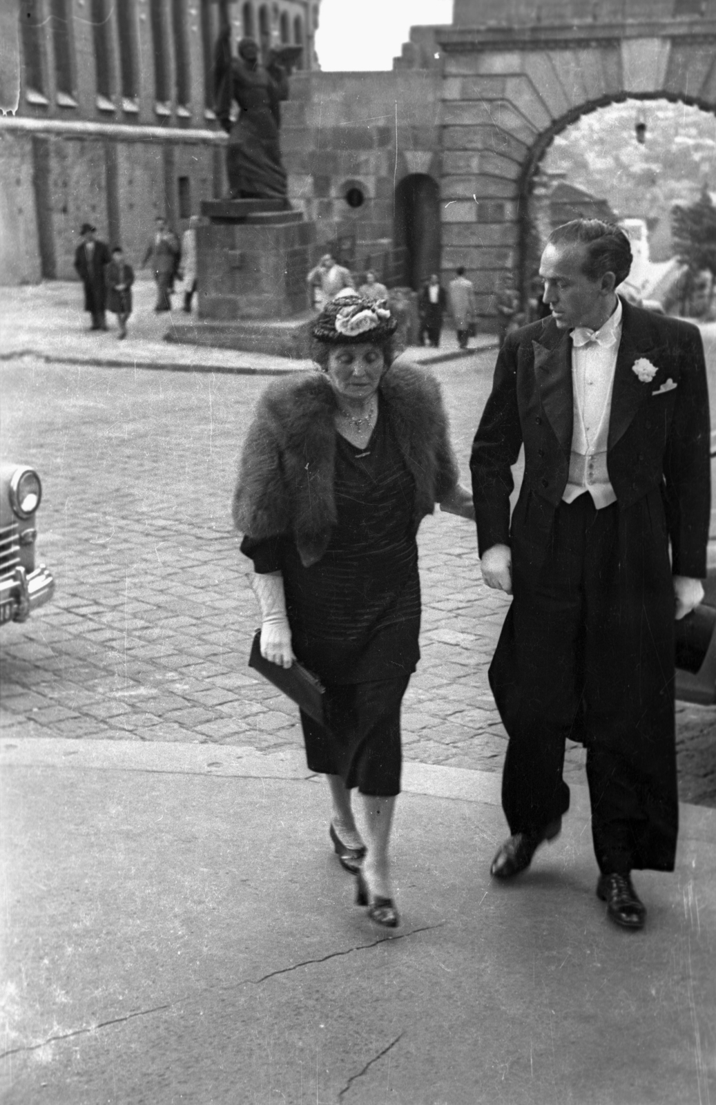 Hungary, Budapest I., Bécsi kapu tér, a felvétel a Budavári Evangélikus templom előtt készült. Háttérben a Bécsi kapu előtt Budavár visszavételének emléke. Balra a Magyar Országos Levéltár épülete., 1953, Hámori Gyula, Budapest, hat, lady, handbag, hat in hand, white tie, fur, gentleman, Fortepan #123439