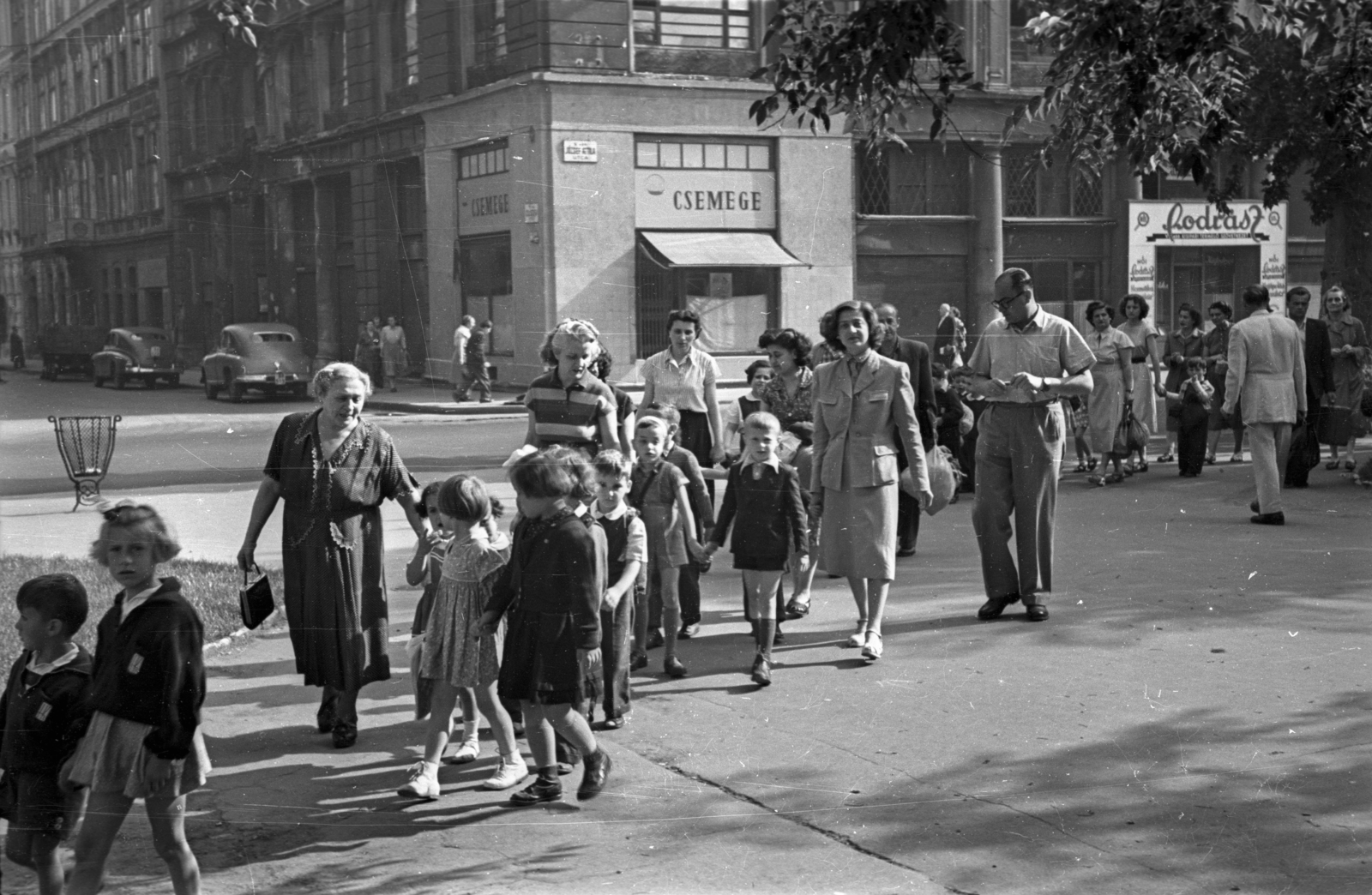 Magyarország, Budapest V., Erzsébet (Engels) tér, szemben a József Attila utca - Sas (Guszev) utca sarok., 1956, Hámori Gyula, Budapest, útkereszteződés, fodrászat, gyerekek, kézenfogva, Csemege vállalat, kosztüm, Fortepan #123677