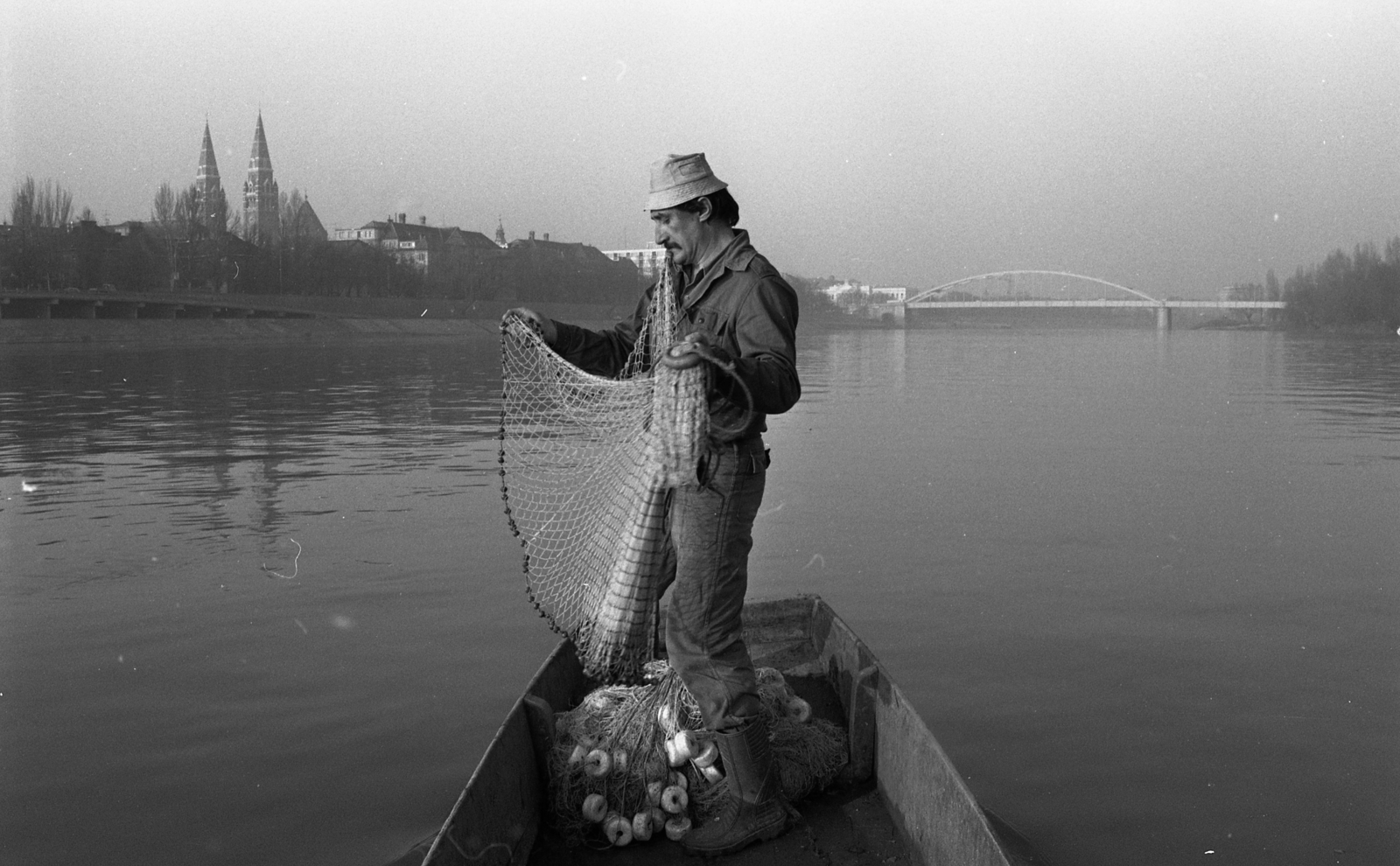 Hungary, Szeged, halász a Tiszán, háttérben a Fogadalmi templom és a Belvárosi híd., 1990, Urbán Tamás, church, bridge, Tisza bridge, boat, fishing, man, wharf, fishing net, steeple, Fortepan #124639