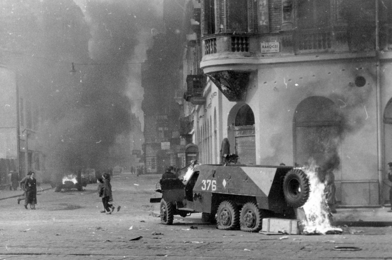Hungary, Budapest VII., Rákóczi út - Akácfa utca sarok. Felgyújtott szovjet BTR-152 páncélozott lövészszállító jármű., 1956, Házy Zsolt, armoured car, revolution, pedestrian, street view, wreck, smoke, fire, combat vehicle, Budapest, Fortepan #12830