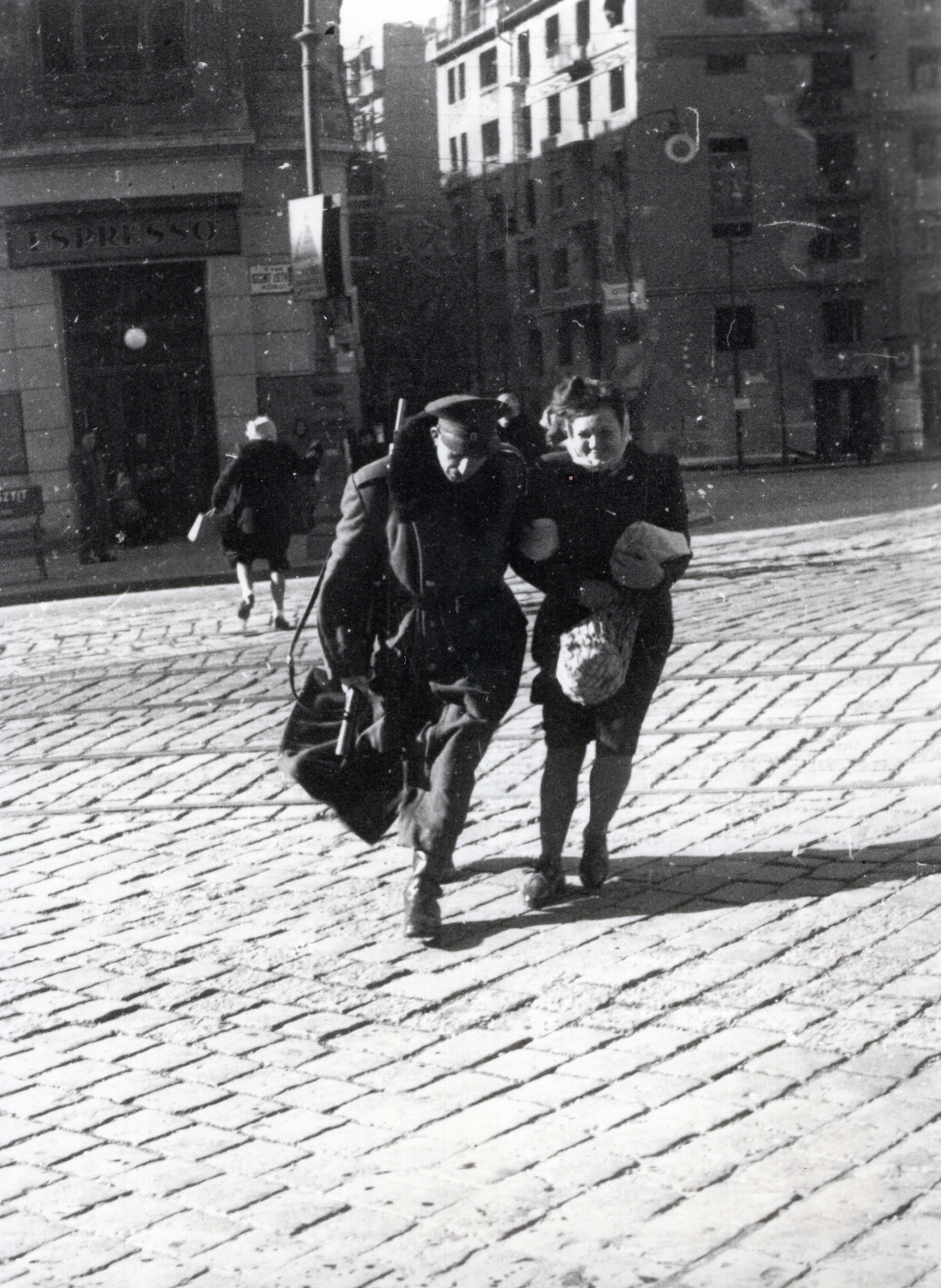 Hungary, Budapest V., Szent István körút, balra az 1. szám, szemben középen a Balassi Bálint (Személynök) utca torkolata, jobbra a Jászai Mari (Rudolf) téren a kiégett bérház, a későbbi ÁVH épülete, ma a Képviselői Irodaház ("Fehér Ház"), 1947, Bauer Sándor, espresso, wind, Budapest, cobblestones, gun, man and woman, street view, Fortepan #128472
