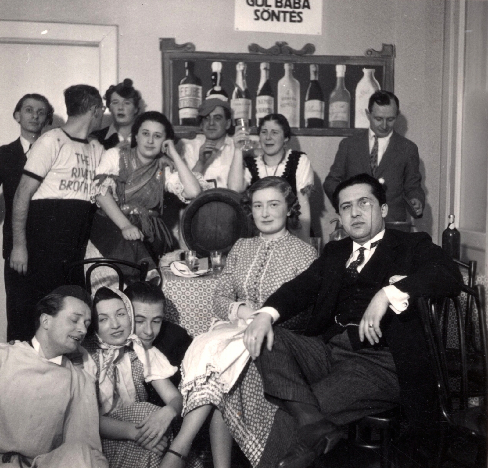 Hungary, Budapest II., Gül Baba utca 36, házavató Péter Andráséknál 1938. január 15-én. Balra fenn Radnóti Miklós költő, lenn Ortutay Gyula néprajzkutató, mellette kendővel Péter Andrásné. Jobb oldalon monoklival Joó Tibor irodalomtörténész., 1938, Paczolay család, tableau, interior, Budapest, odd one out, looking back, barrel, fresco, Fortepan #131499