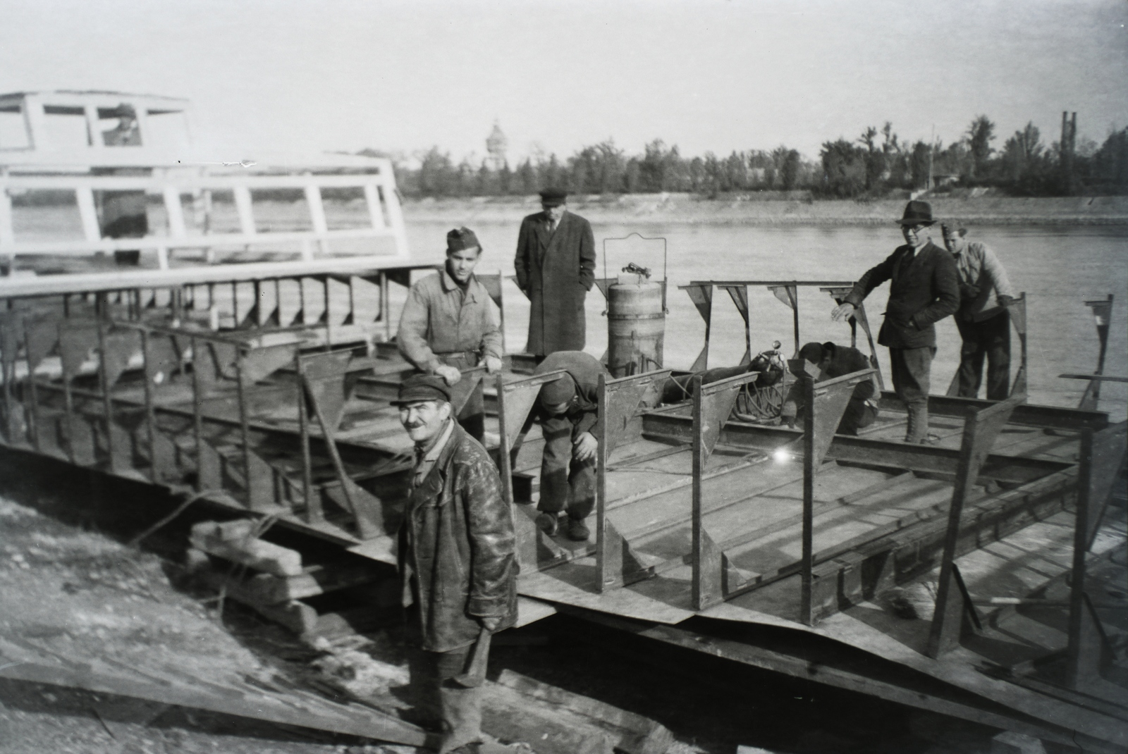 Hungary, Budapest III., Árpád fejedelem útja 50., Asboth hajóépítő telep, az AT 50/2 légcsavaros hajó építés közben a sólyán, háttérben a Margit-sziget és a víztorony. Leltári jelzet: MMKM TFGY 2017.5.7, 1946, Magyar Műszaki és Közlekedési Múzeum / Történeti Fényképek Gyűjteménye / Asboth Oszkár gyűjteménye, hat, leather jacket, cap, shipbuilding industry, Budapest, Fortepan #132143