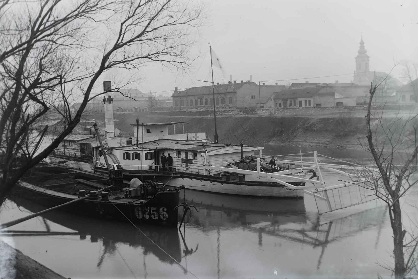 Magyarország, Óbuda, Budapest III., Óbudai Hajógyár, Duna-ág a Hajógyári-sziget mellett, DDSG Traisen oldalkerekes vontató gőzhajó (épült: 1884.). Háttérben a Szent Péter és Pál-templom és a szentendrei HÉV villamosított vonala. Leltári jelzet: N223, 1915, Magyar Műszaki és Közlekedési Múzeum / Történeti Fényképek Gyűjteménye / Óbudai Hajógyár gyűjteménye, Budapest, Fortepan #133167