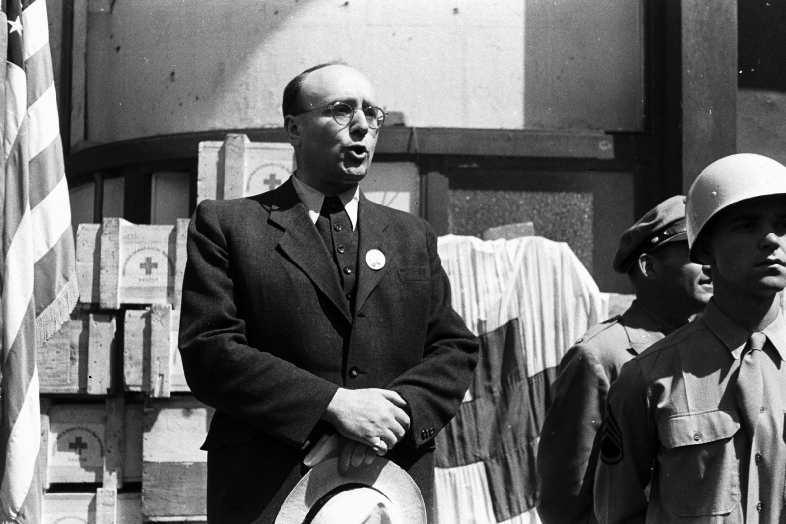 Hungary, Budapest V., Kossuth Lajos tér 18., a felvétel az Egyesült Államok katonai missziójának székháza előtt az amerikai magyarok gyógyszerajándékának átadásakor készült. Beszédet mond a Nemzetközi Vöröskereszt részéről Hans Weyermann kiküldött., 1945, Chuckyeager tumblr, flag, glasses, helmet, chest, American soldier, Budapest, hat in hand, badge on a lapel, Fortepan #142684