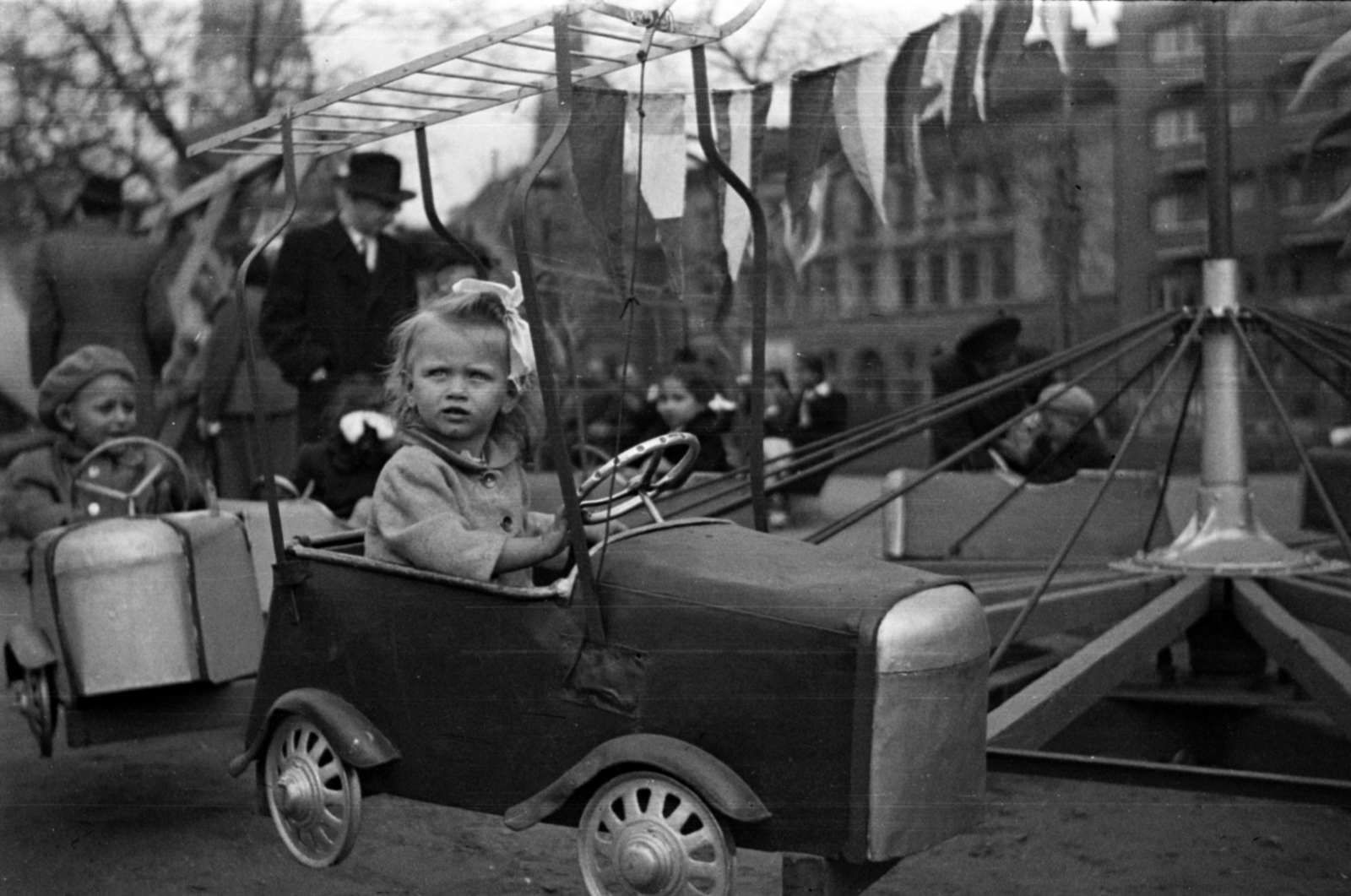 Hungary, Budapest VIII., II. János Pál pápa (Köztársaság) tér, a háttérben balra az OTI székház tornya és a Dologház utca - Kun utca sarkon a Tűzoltóparancsnokság épületének a tornya., 1950, Barbjerik Ferenc, Budapest, girl, ribbon, model car, carousel, pedal car, Fortepan #148338