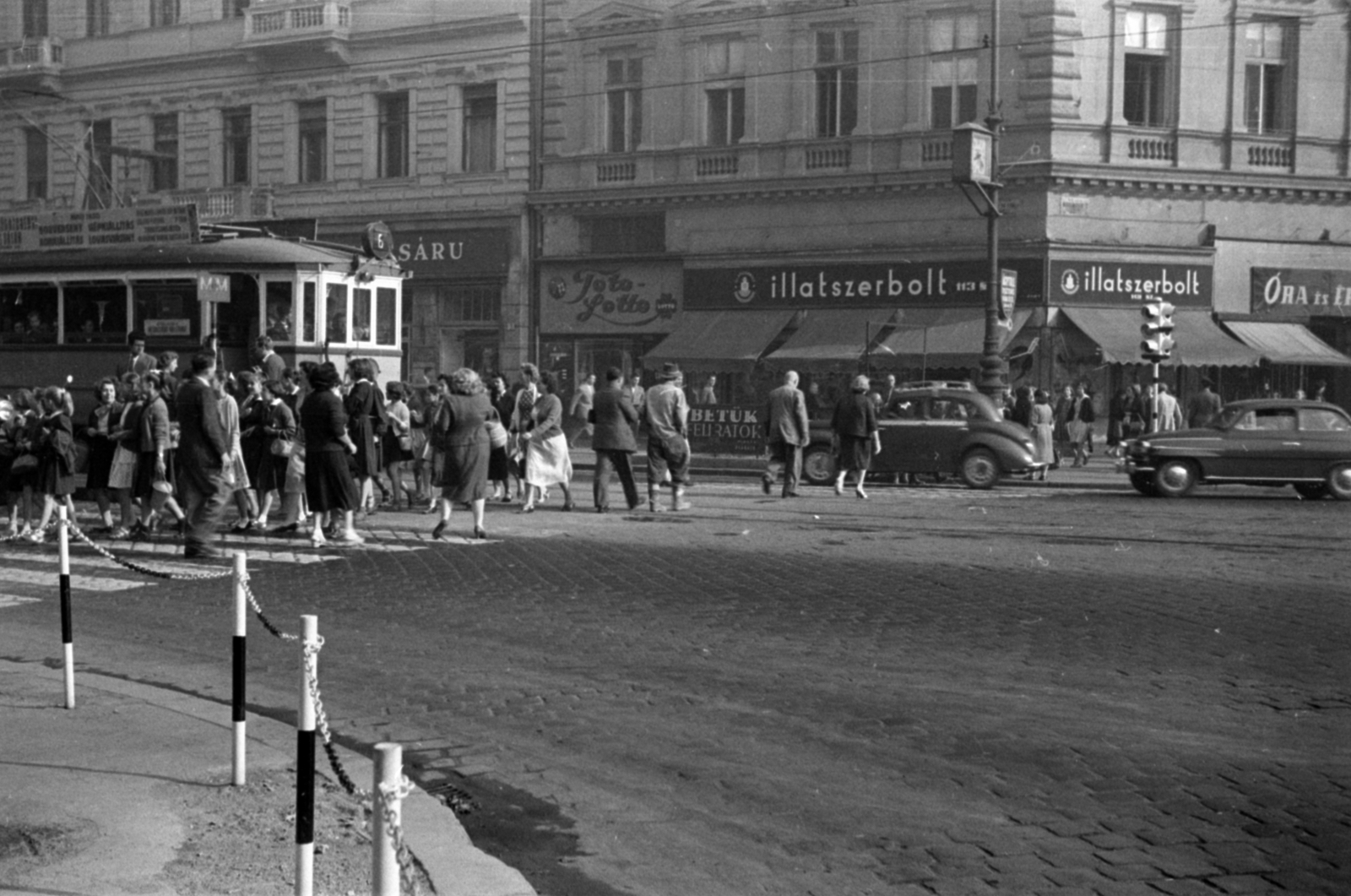 Hungary, Budapest VI., Oktogon (November 7. tér) szemben a 4. számú épület Teréz (Lenin) körúti oldala., 1955, Barbjerik Ferenc, Budapest, public clock, railing, sign-board, automobile, tram, awning, crosswalk, Fortepan #148410