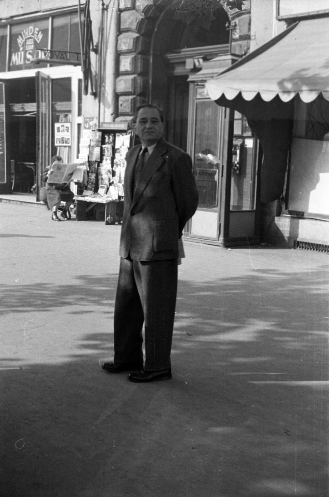 Hungary, Budapest VI., Oktogon (November 7. tér) 1., balra a Savoy kávéház., 1955, Barbjerik Ferenc, Budapest, hands behind the back, phone booth, tie, suit, reading, awning, newsstand, Fortepan #148411