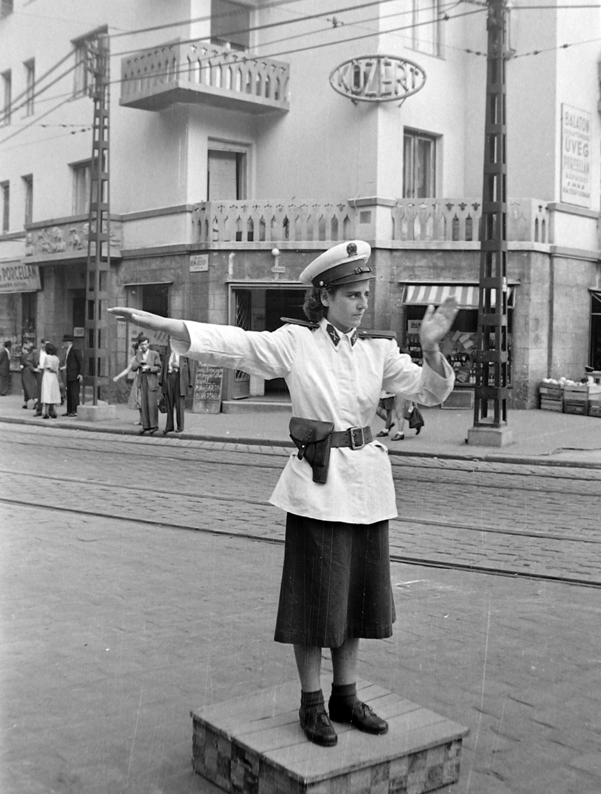 Magyarország, Budapest II., Margit körút (Mártírok útja), a forgalomírányító rendőr mögött a Bem József utca - Horvát utca sarokán álló ház látható., 1951, Magyar Rendőr, neonreklám, rendőr, erkély, pisztoly, utcanévtábla, rendőrdobogó, pisztolytáska, Budapest, élelmiszerbolt, rendőrnő, forgalomirányítás, egyenruha, tányérsapka, Közért Vállalat, napellenző, Fortepan #16687
