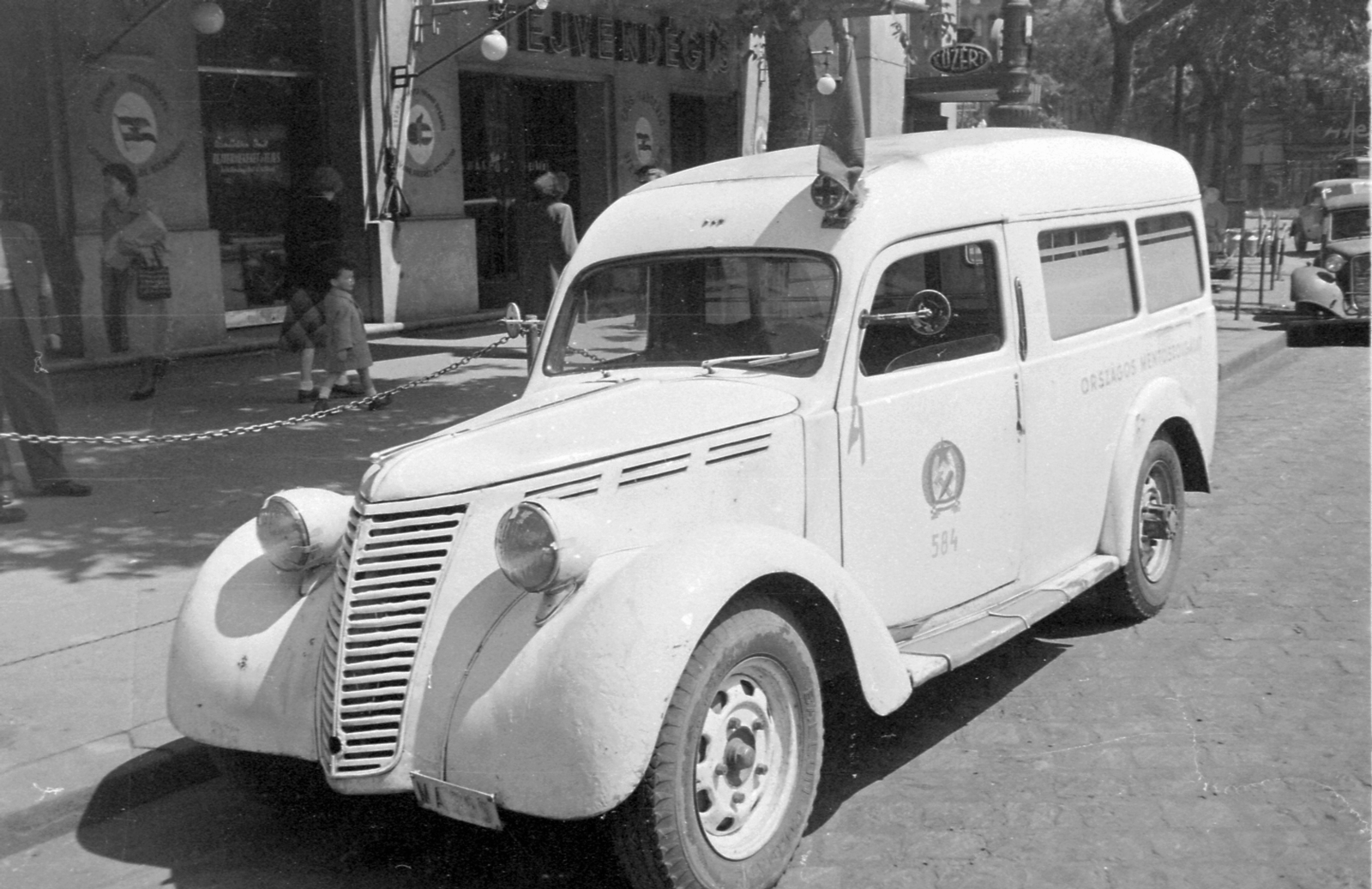 Hungary, Budapest XIII., Nyugati (Marx) tér a Szent István körút és a Váci út között. Fiat 1100 mentőautó, a háttérben a Westend-ház üzletei., 1952, Magyar Rendőr, neon sign, Fiat-brand, Italian brand, ambulance, crest, automobile, number plate, Budapest, grocery store, Rákosi crest, Fortepan #16768