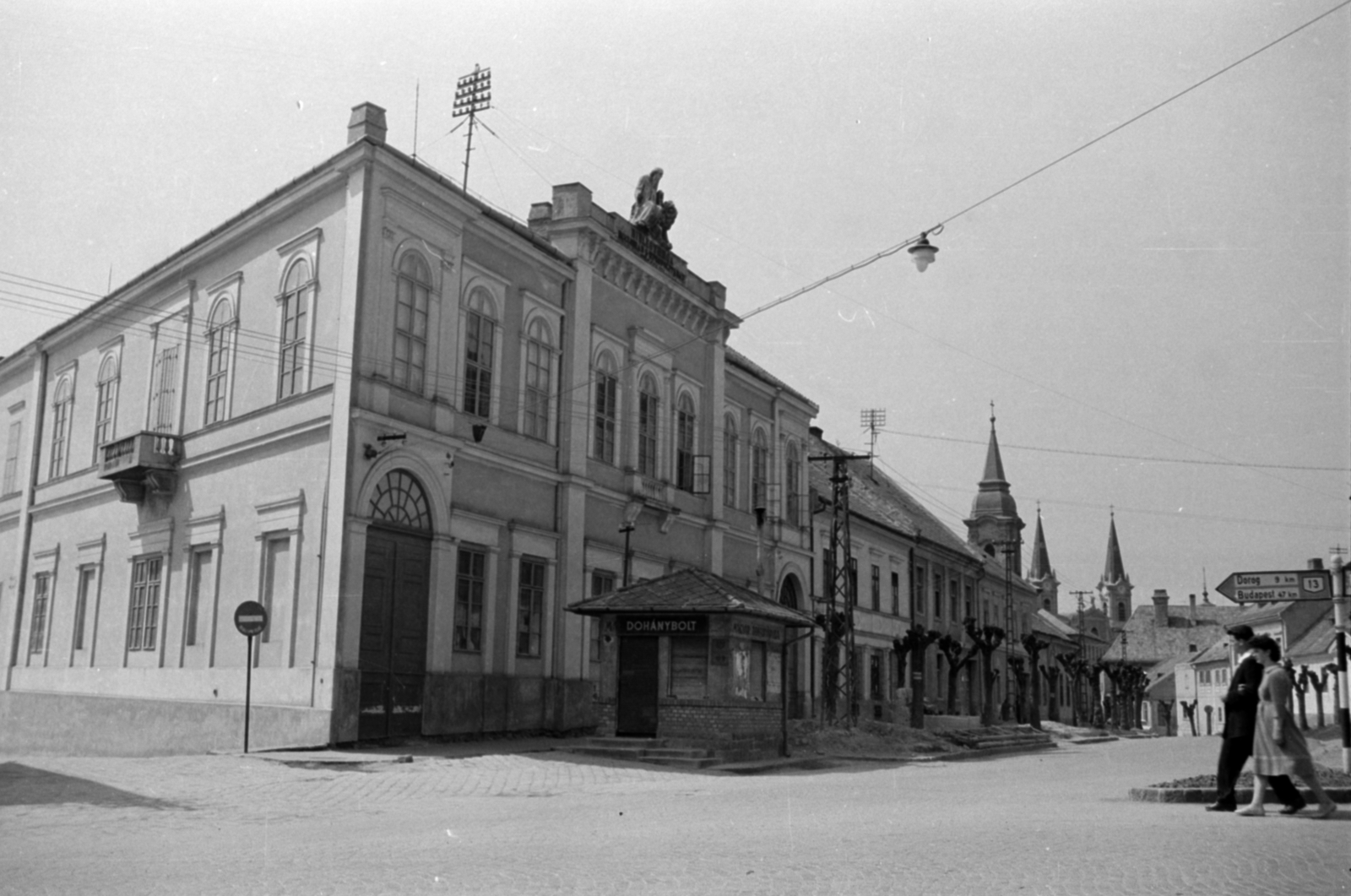 Hungary, Esztergom, Bajcsy-Zsilinszky út (11-es főút), balra a Liszt Ferenc utca torkolata, jobbra a Pázmány Péter utca (ekkor ez is Bajcsy-Zsilinszky út). A saroképület a Főszékesegyházi Könyvtár (Bibliothéka). A távolban a Szatmári Irgalmasnővérek Zárdatemploma és a Loyolai Szent Ignác-templom., 1960, Sattler Katalin, tobacco shop, cornerhouse, Fortepan #171454