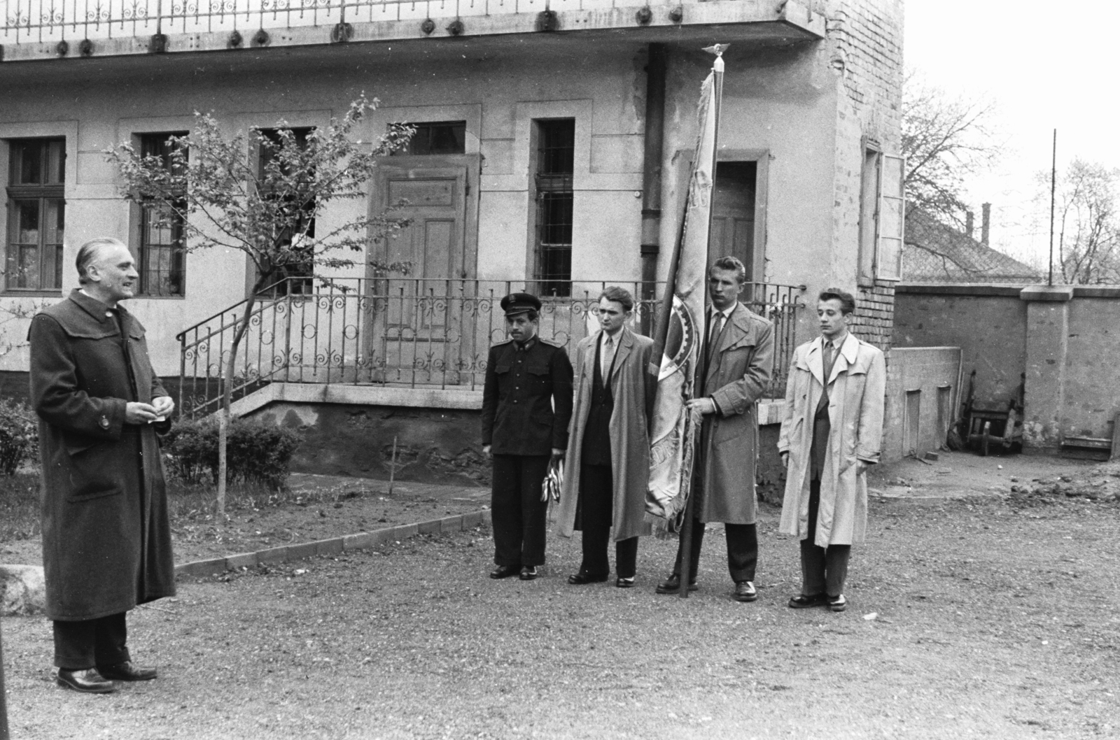 Hungary, Szolnok, Gutenberg tér, a Közlekedési Műszaki Egyetem (1952-1957) kollégiuma ideiglenes helyén, a Művésztelep egyik épületében. Balra dr. Turányi István, az egyetem igazgatója., 1954, Chuckyeager tumblr, flag, trench coat, men, festive, yard, student dorm, Fortepan #176453