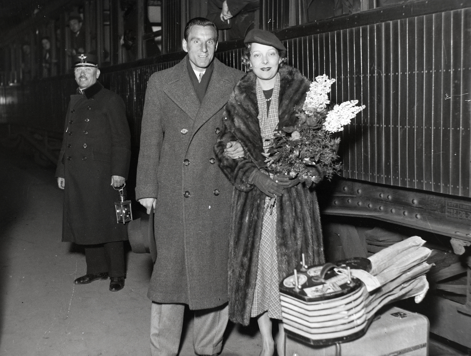 Hungary, Budapest VI., a Nyugati pályaudvar csarnoka. Fred Perry angol világbajnok teniszező és felesége, Mary Lawson angol fílmszínésznő., 1936, Bojár Sándor, light, fur coat, bouquet, railroader, tennis rackets, train, winter coat, Budapest, Fortepan #177180