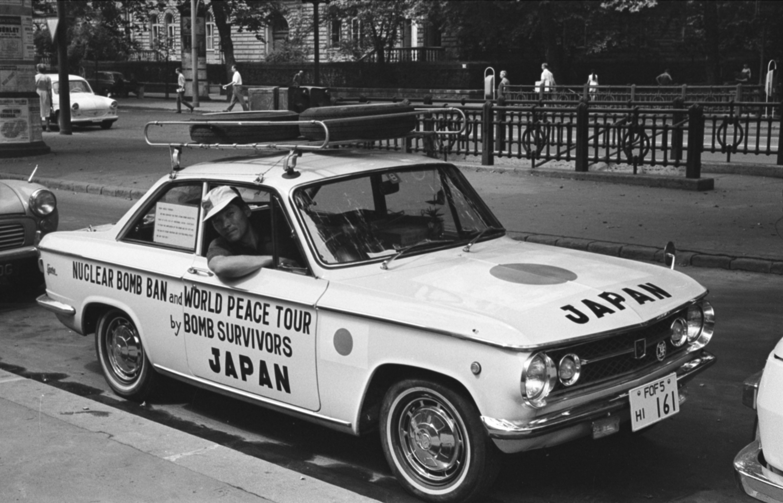 Hungary, Budapest VI., Andrássy út (Népköztársaság útja) a Hopp Ferenc Kelet-ázsiai Művészeti Múzeum előtt. A világkörüli úton lévő japán Masashi Nii, aki átélte Hirosima bombázását, és az életét az atomfegyverek elleni harcnak szentelte., 1967, Bojár Sándor, Budapest, Mazda-brand, spare wheel, number plate, subway station, Fortepan #179881