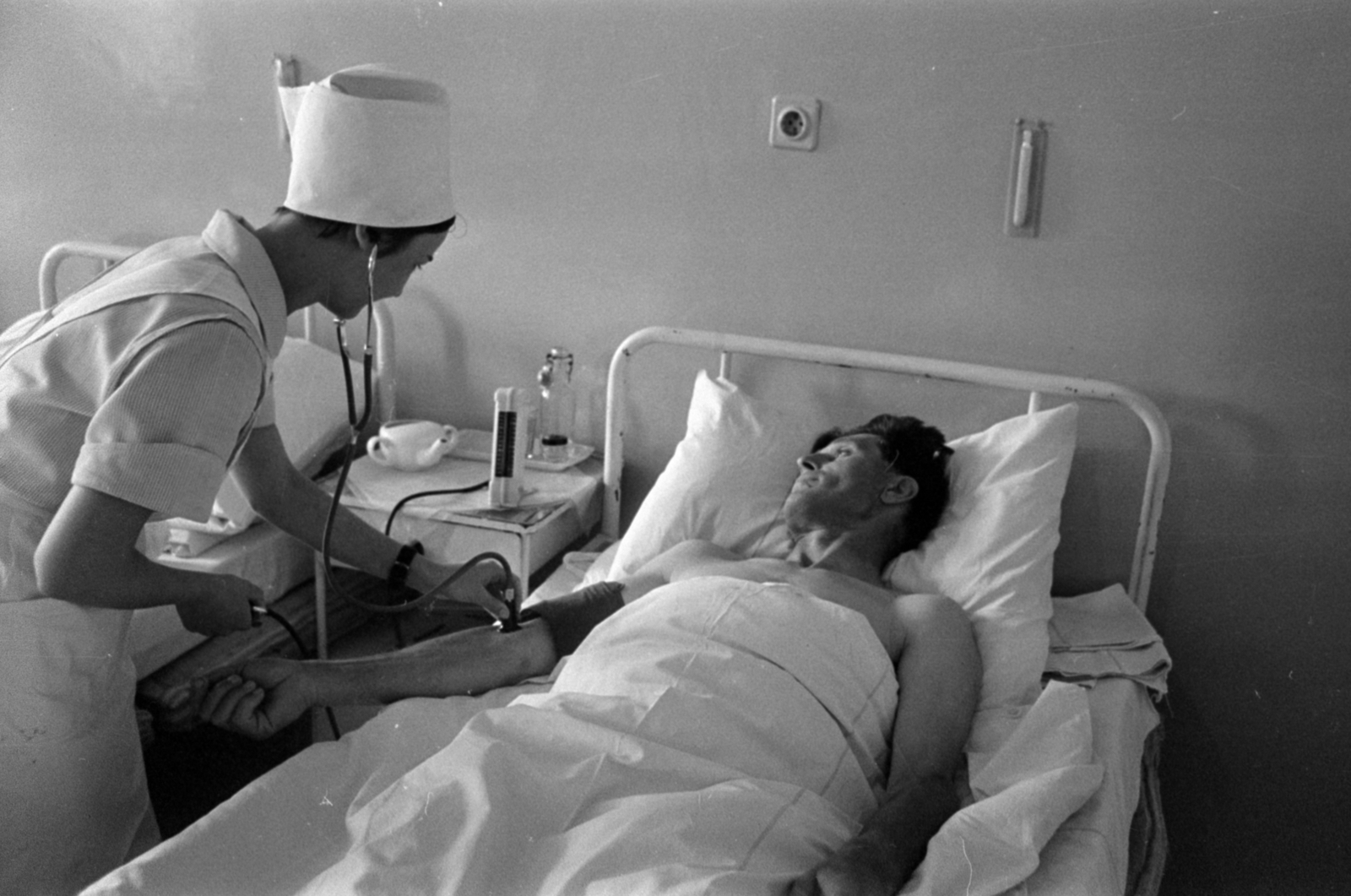 Hungary, Hatvan, az ecsedi szénbánya külszíni fejtésénél súlyos sérüléseket szenvedett dömpervezető a hatvani kórházban., 1966, Bojár Sándor, nurse, iron bed, blood pressure monitor, physical examination, Fortepan #180248