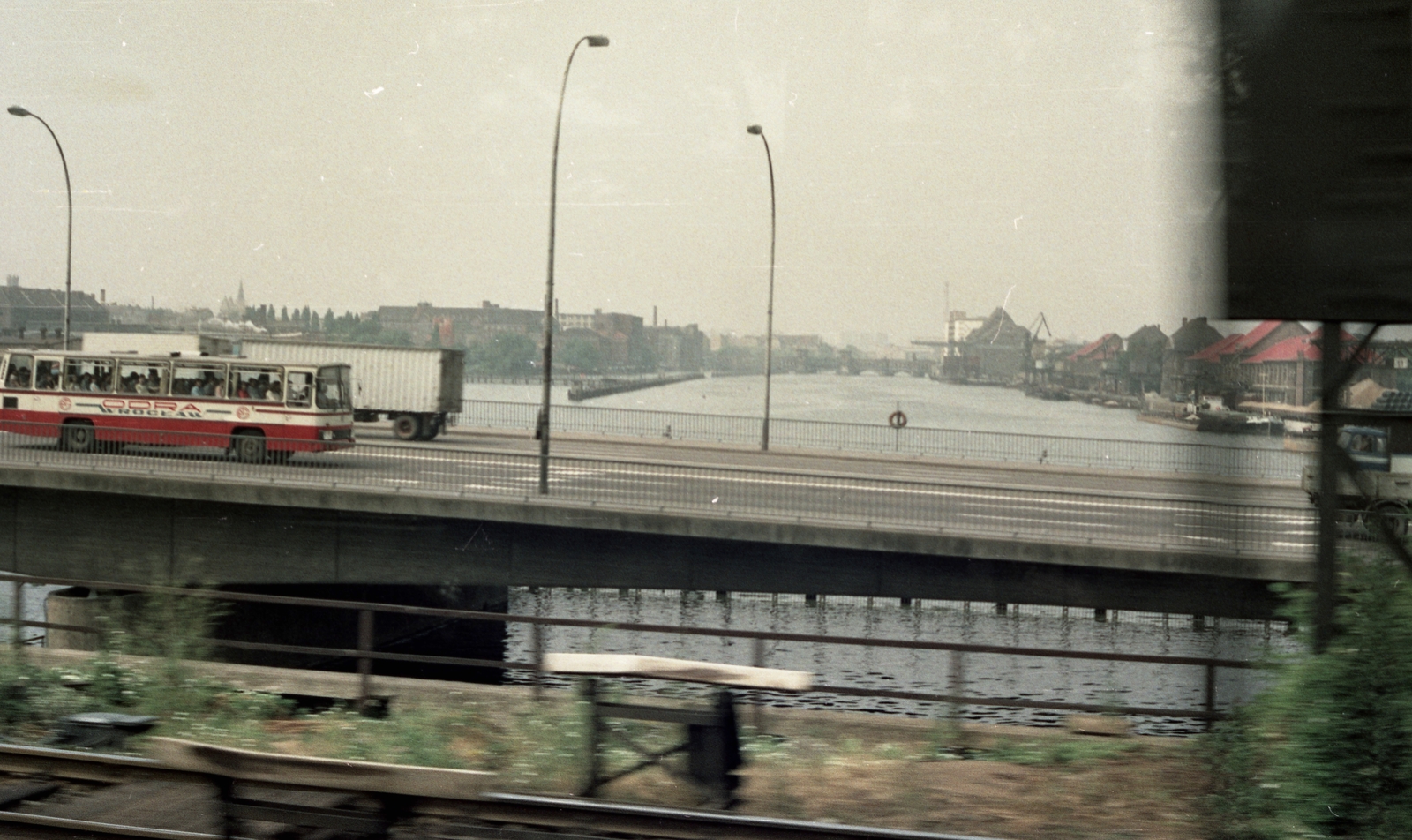 Németország, Berlin, Kelet-Berlin, a Spree folyó a Ringbahnbrücke Oberspree-n áthaladó vonat ablakából nézve. Előtérben az Elsenbrücke, a távolban az Oberbaumbrücke körvonalazódik., 1983, Gulyás Zsuzsa, színes, NDK, Kelet-Berlin, autóbusz, Fortepan #186518