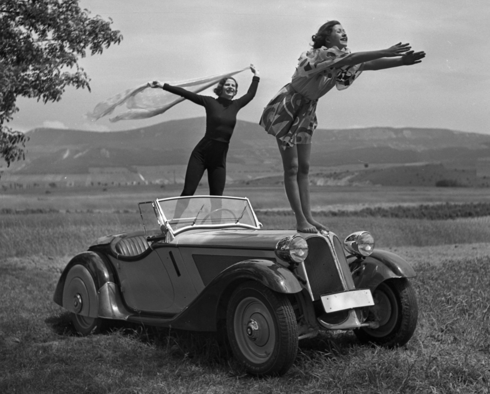 Hungary, Solymár, BMW 319 Roadster személygépkocsi. Háttérben a Kevély-hegycsoport (a Kis-Kevély, a Nagy-Kevély és az Ezüst-Kevély)., 1936, Szöllősy Kálmán, German brand, BMW-brand, posture, automobile, wind, convertible, girls'n'cars, spread out arms, standing on a car, Fortepan #18781