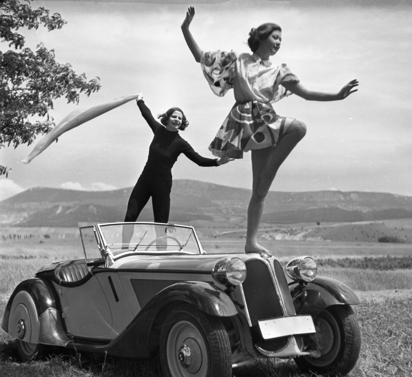 Hungary, Solymár, BMW 319 Roadster személygépkocsi. Háttérben a Kevély-hegycsoport (a Kis-Kevély, a Nagy-Kevély és az Ezüst-Kevély)., 1936, Szöllősy Kálmán, fashion, German brand, women, BMW-brand, posture, automobile, convertible, girls'n'cars, spread out arms, standing on a car, one leg standing, Fortepan #18785