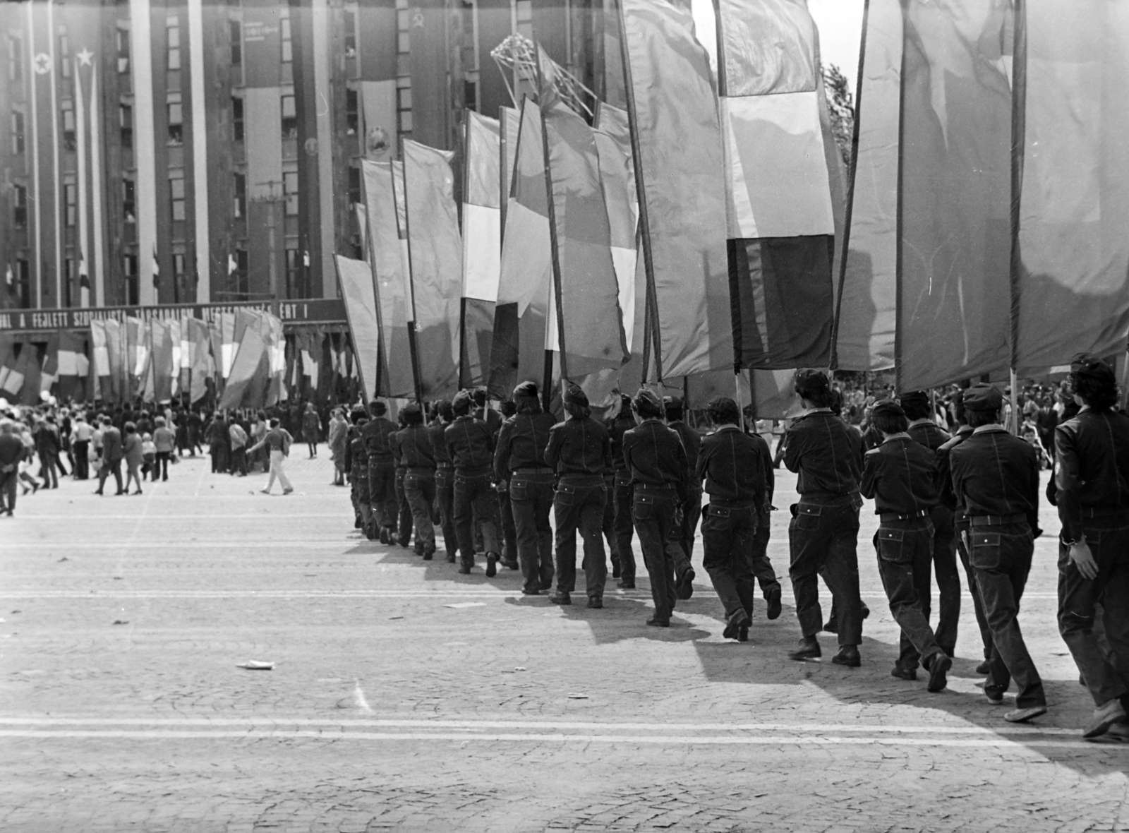 Magyarország, Budapest XIV.,Budapest VI., Ötvenhatosok tere (Felvonulási tér), május 1-i felvonulás végén elhagyják a teret a zászlótartó fiatalok. Háttérben a Dózsa György út 84., a MÉMOSZ (Magyarországi Építőipari Munkások Országos Szövetsége) székháza., 1978, Orosz István, Budapest, Fortepan #188997