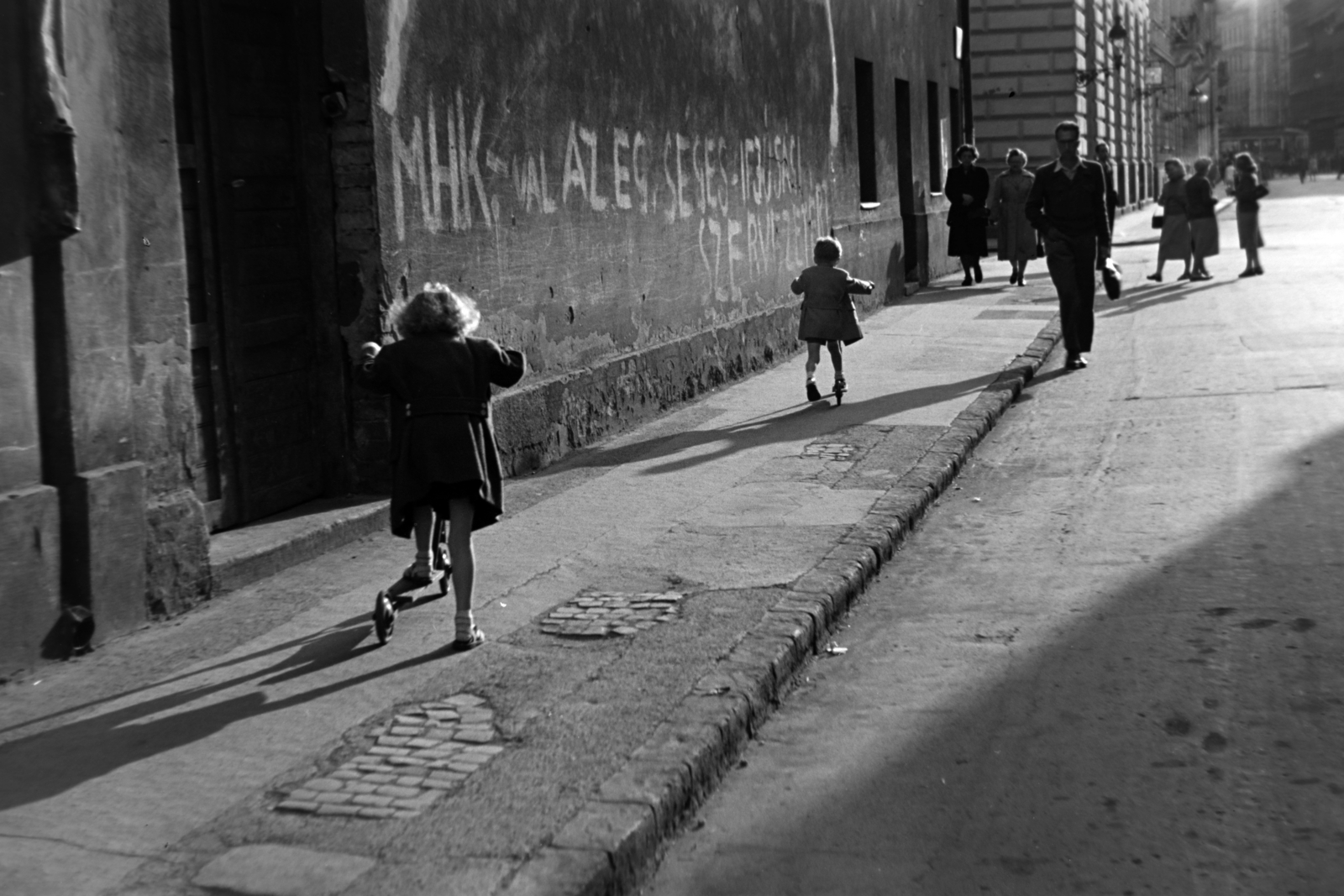 Hungary, Budapest VIII., Kis Stáció utca a Harminckettesek tere felé nézve, balra a Kisfaludy utca torkolata., 1954, Kriss Géza, Budapest, girl, slogan, scooter, graffiti, pavement, MHK movement, Fortepan #191809
