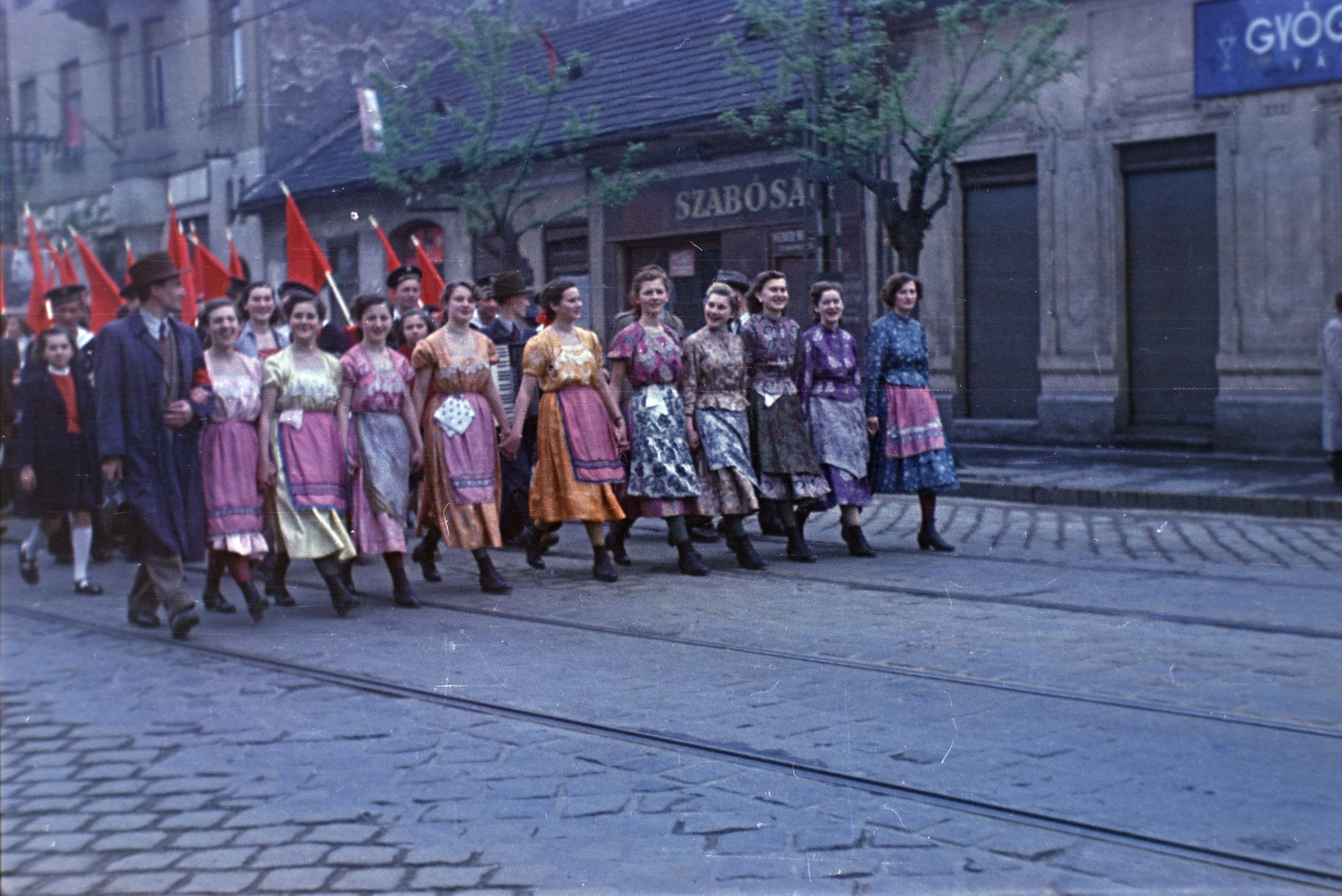Hungary, Budapest IV., Árpád út, háttérben a 42., 44. és 46. számú ház., 1955, Kriss Géza, flag, march, Budapest, colorful, tailors, girls, youth, trench coat, hold hands, folk costume, Fortepan #191868