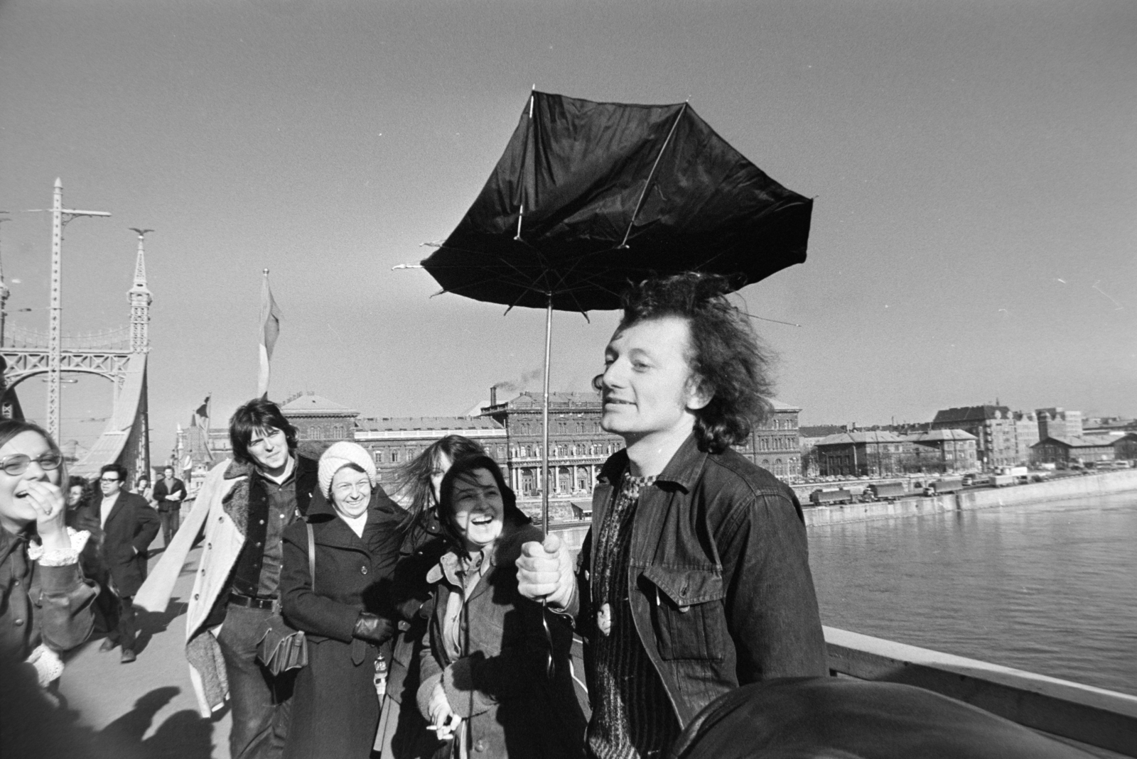 Hungary, Budapest IX., Szabadság híd, háttérben a Fővám (Dimitrov) tér, Marx Károly Közgazdaságtudományi Egyetem (később Corvinus Egyetem). Középen fehér sapkában Torday Alíz az MTV szerkesztője, jobbra a Bedobás kitalálója Dozvald János fotóművész, újságíró. A felvétel az évente megtartott Bedobás / felesleges tárgyak Dunába dobása alkalmával készült., 1977, Gábor Viktor, Budapest, Fortepan #194200