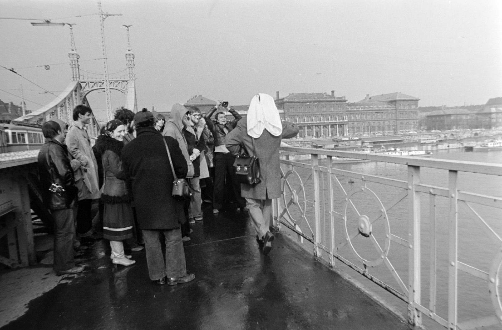 Magyarország, Budapest IX., Szabadság híd, háttérben a Fővám (Dimitrov) tér, Marx Károly Közgazdaságtudományi Egyetem (később Corvinus Egyetem). A felvétel az évente megtartott Bedobás / felesleges tárgyak Dunába dobása alkalmával készült., 1979, Gábor Viktor, Budapest, Fortepan #194453