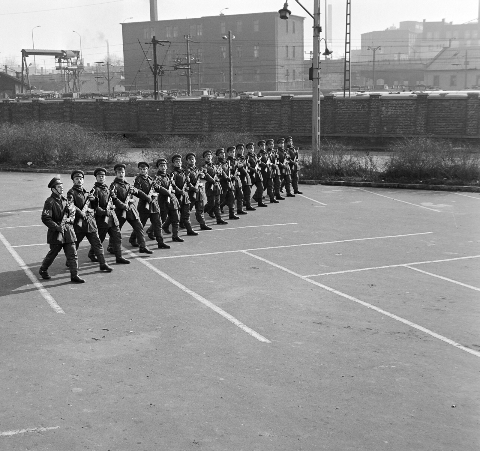 Hungary, Budapest XIV., Dózsa György út, április 4- díszszemlére készülő katonák a Népstadion melletti parkolóban. Jobbra a Keleti pályaudvar külső vágányai és a Kerepesi úti "Százlábú híd" mögött az Országos (később Taurus) Gumiipari Vállalat épületei., 1975, Bojár Sándor, Budapest, Kalashnikov, machine gun, Fortepan #195197