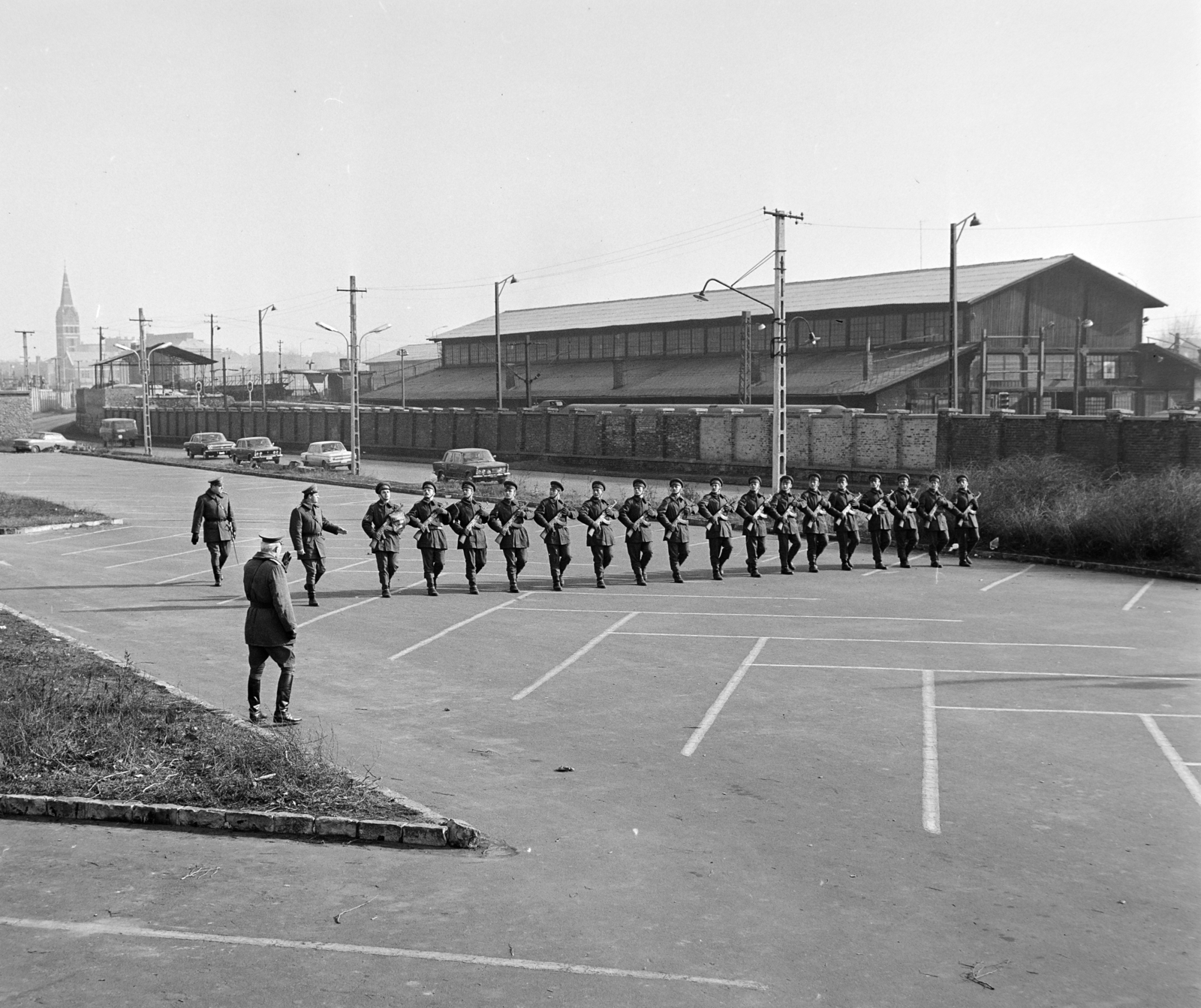 Hungary, Budapest XIV., Dózsa György út, április 4- díszszemlére készülő katonák a Népstadion melletti parkolóban. Távolban balra a Kerepesi úti Szent Teréz-templom, a kerítés mögött a Keleti pályaudvar egyik műhelycsarnoka., 1975, Bojár Sándor, Budapest, Fortepan #195198